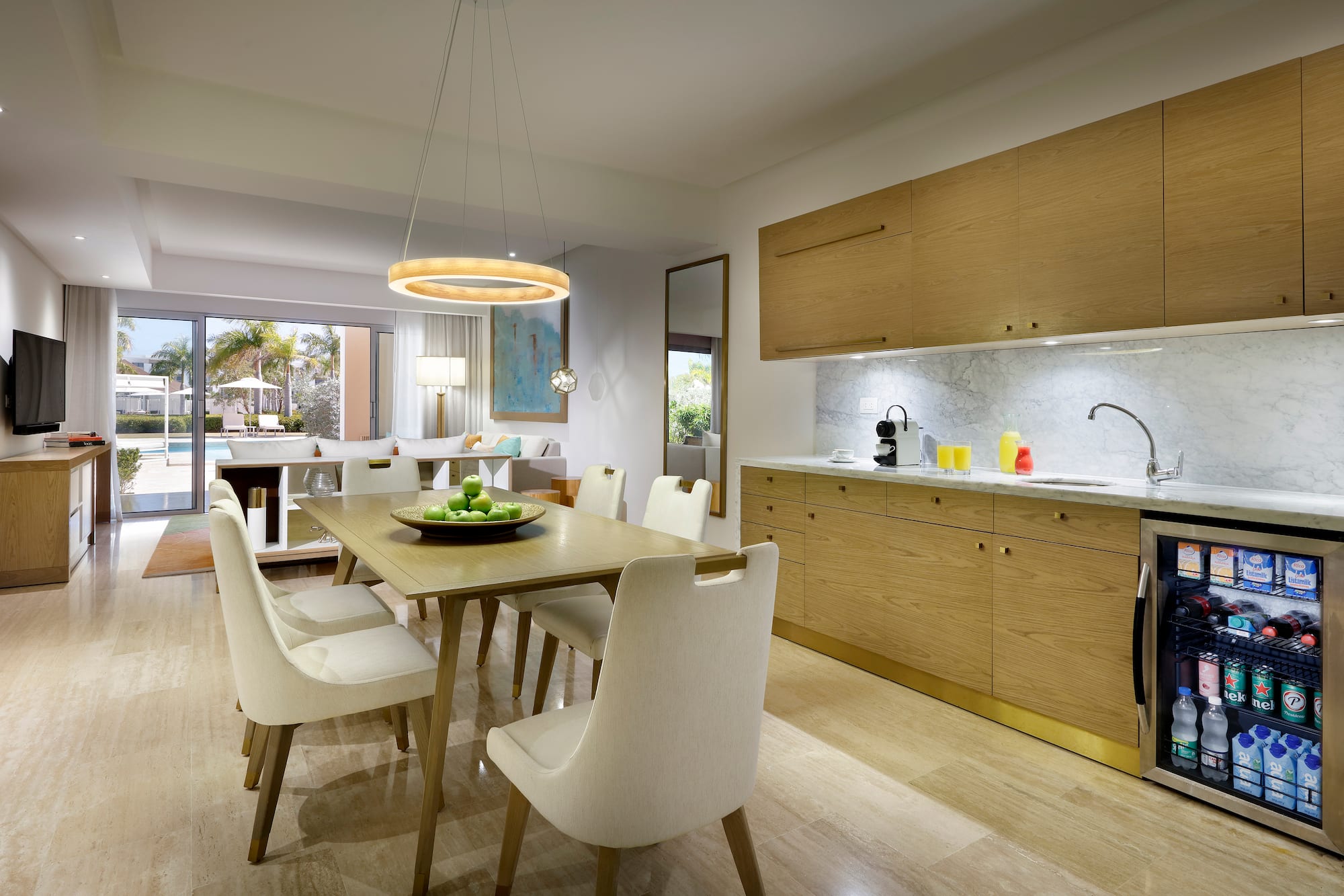 Modern resort suite: dining, kitchenette, living area, and pool view.