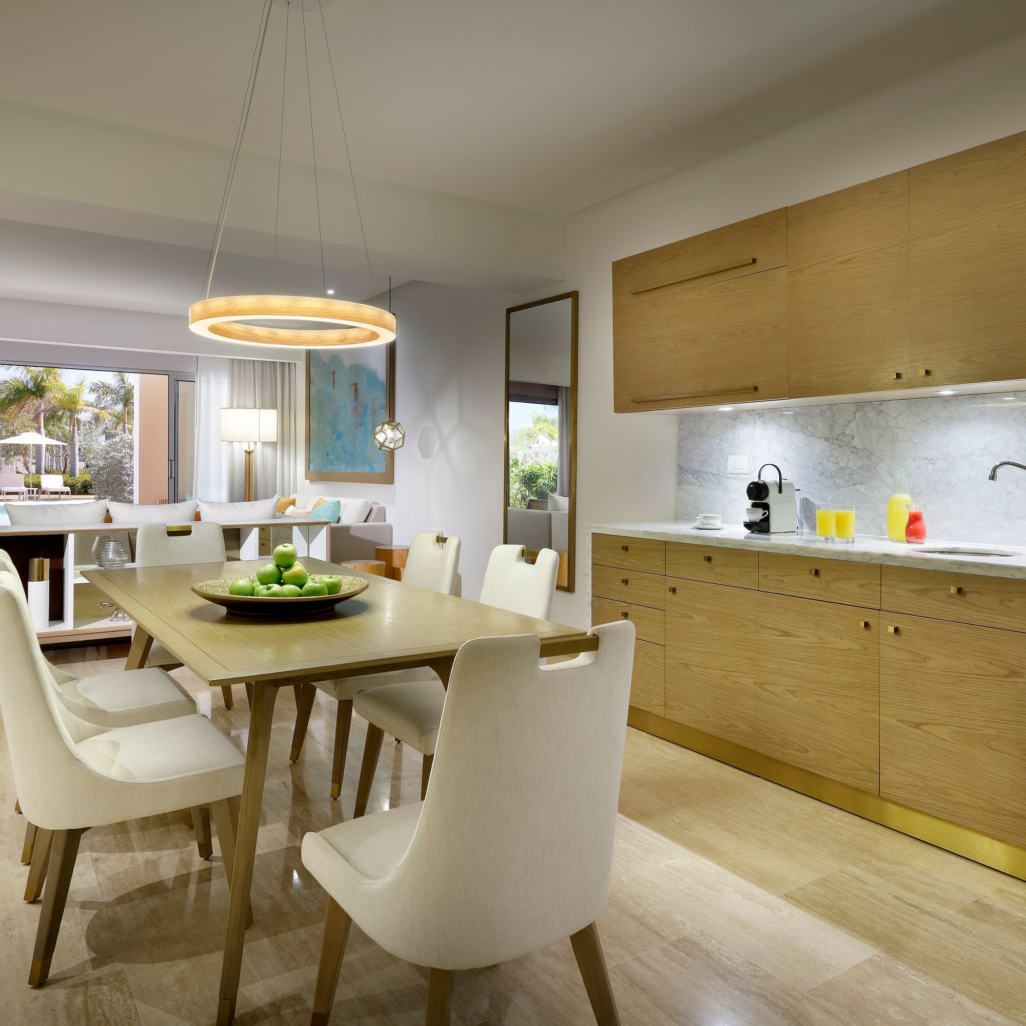 Modern resort suite: dining, kitchenette, living area, and pool view.