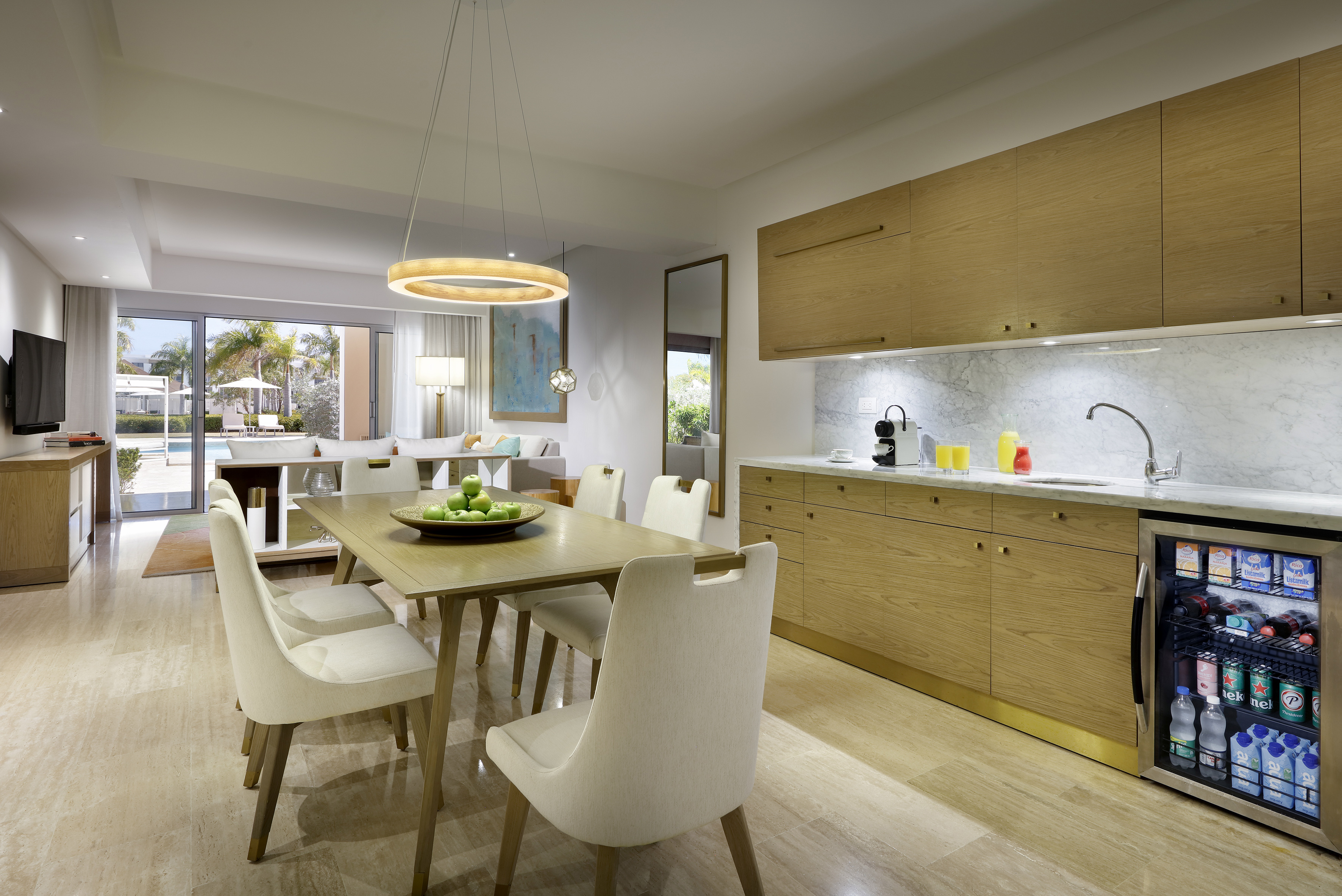 Modern resort suite: dining, kitchenette, living area, and pool view.