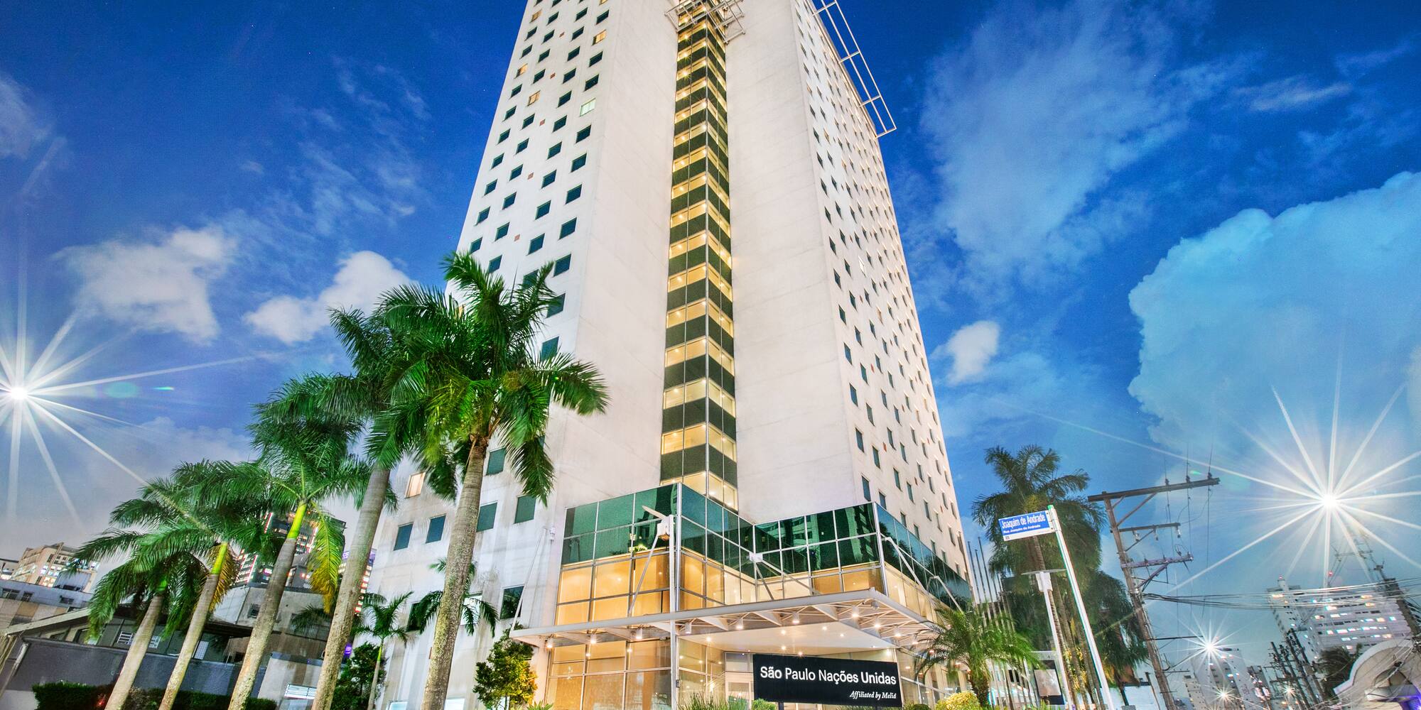 São Paulo Nações Unidas hotel at night with illuminated facade and palm trees.