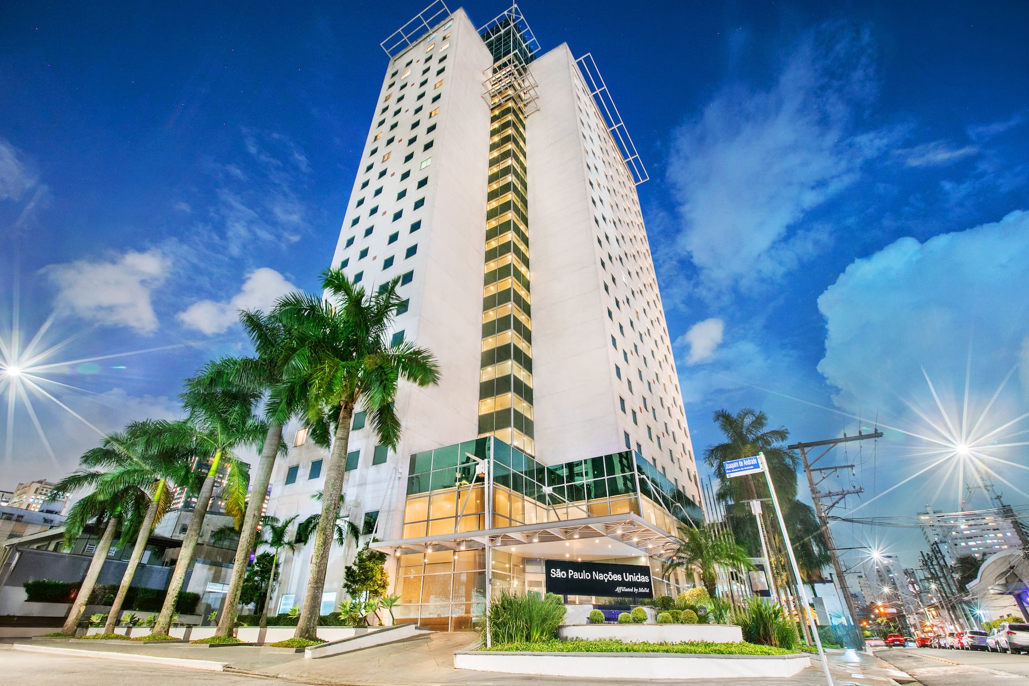 São Paulo Nações Unidas hotel at night with illuminated facade and palm trees.