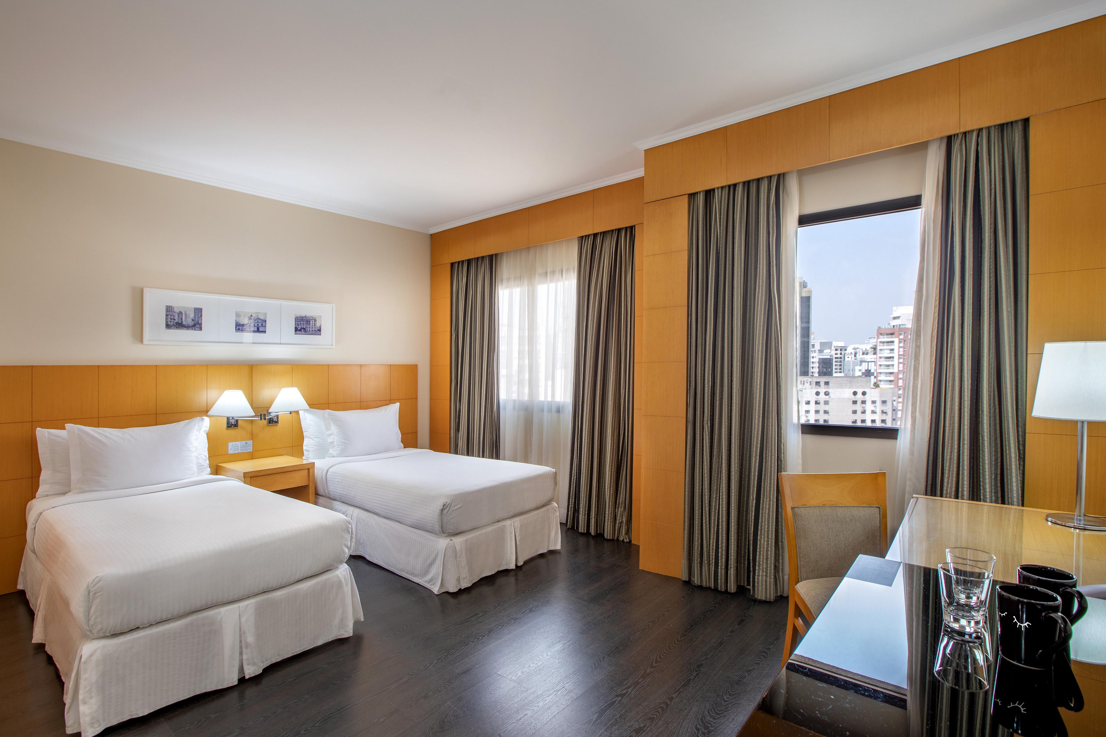 Hotel twin room with city view, two beds, wooden headboard, and desk.