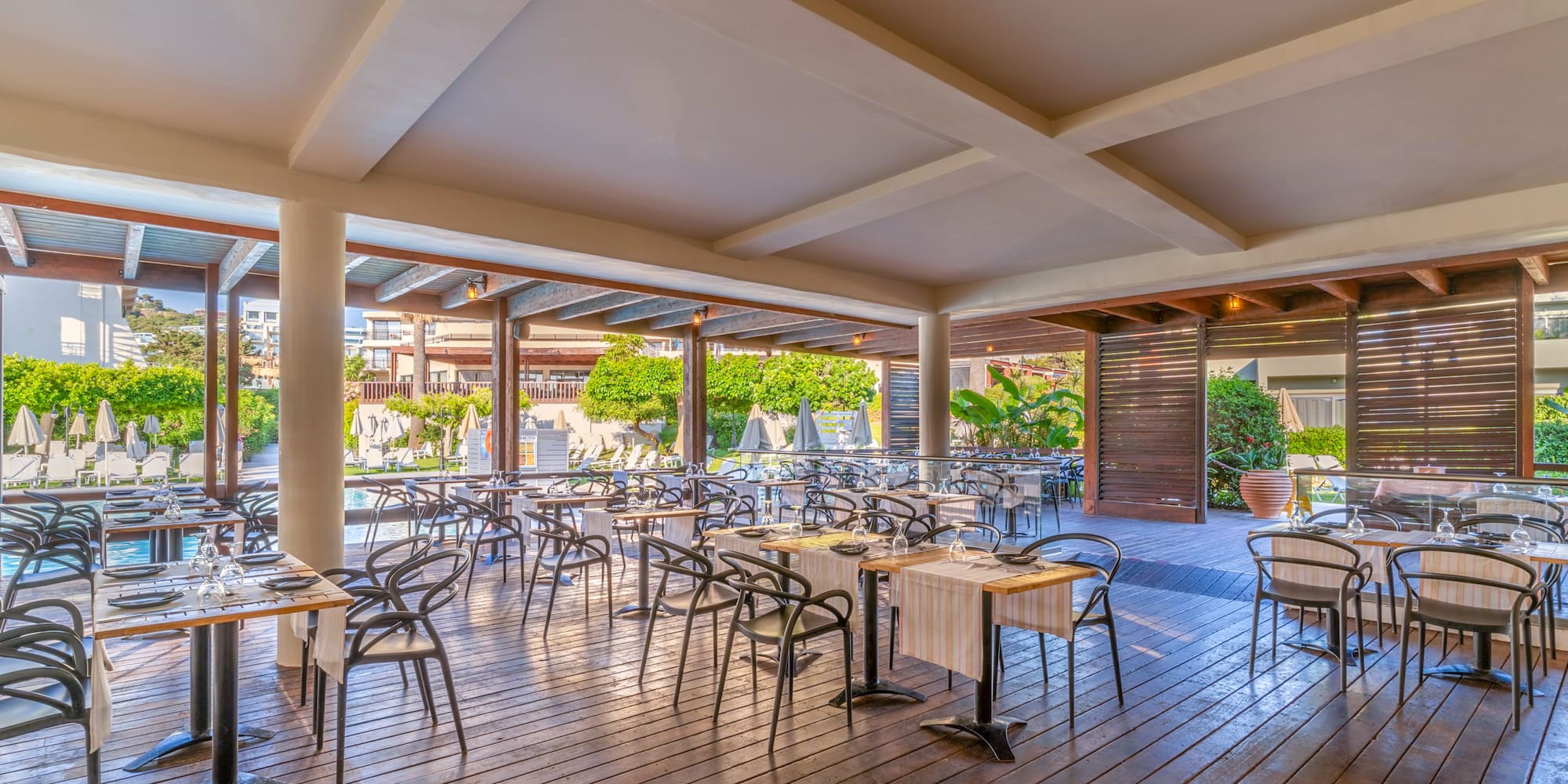 Poolside resort restaurant with set tables on a wooden deck.