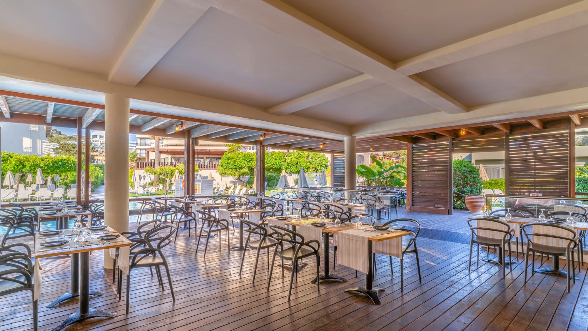 Poolside resort restaurant with set tables on a wooden deck.