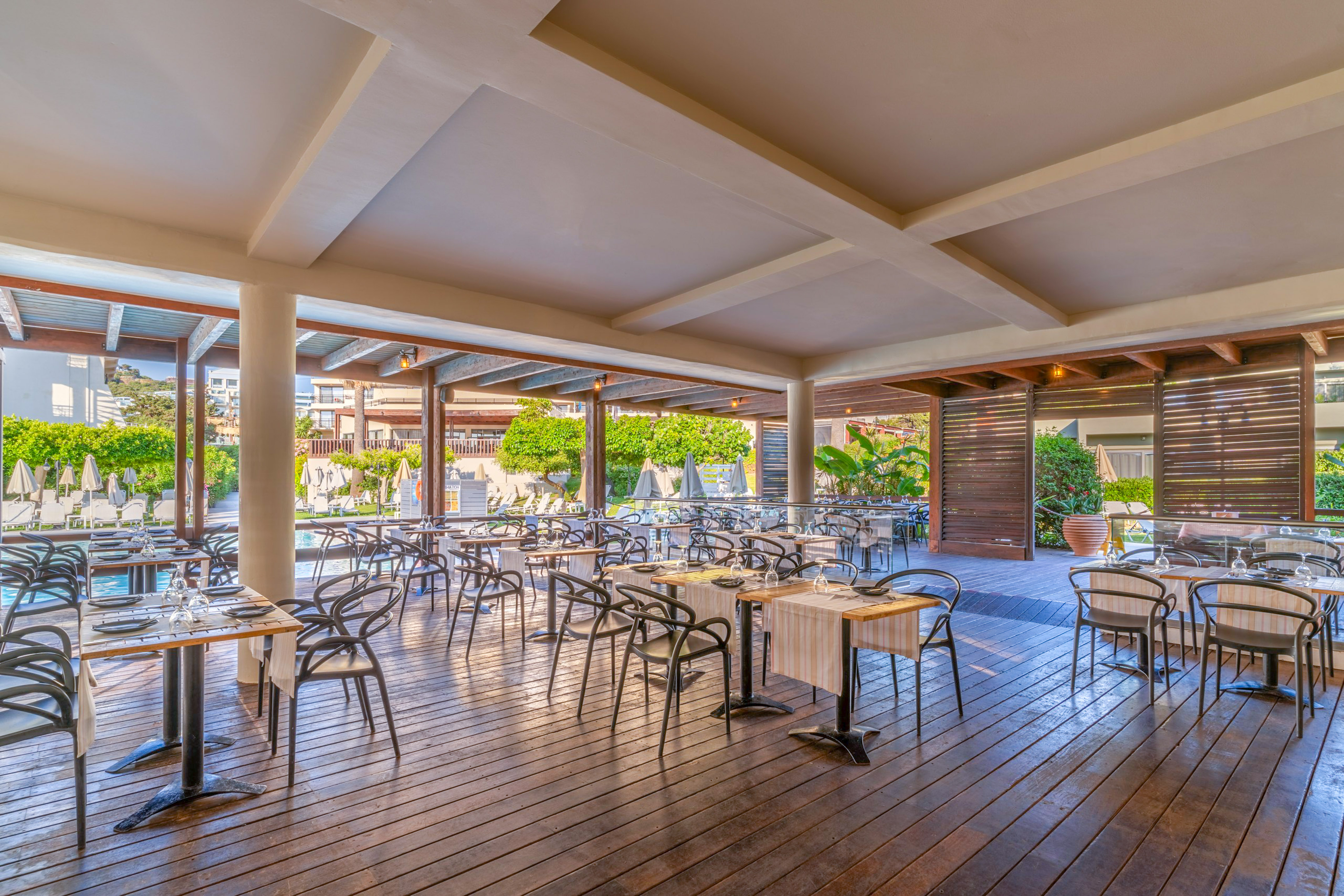 Poolside resort restaurant with set tables on a wooden deck.