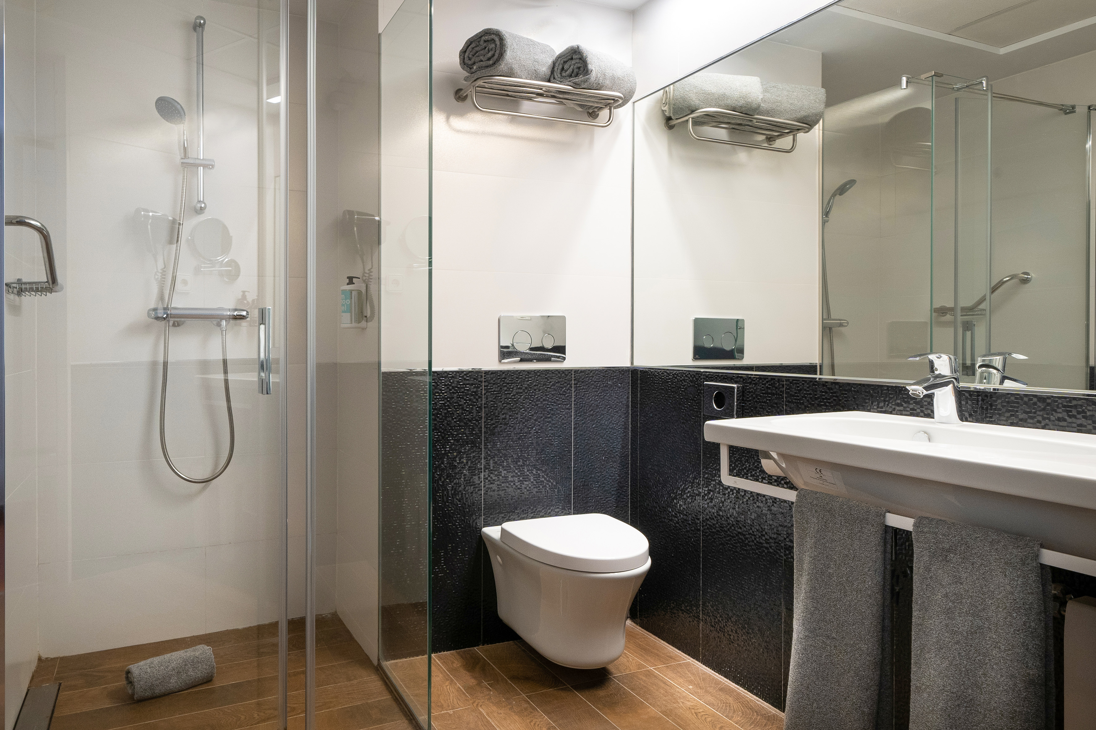 Modern bathroom with walk-in shower, wall-mounted toilet, sink, and towels.