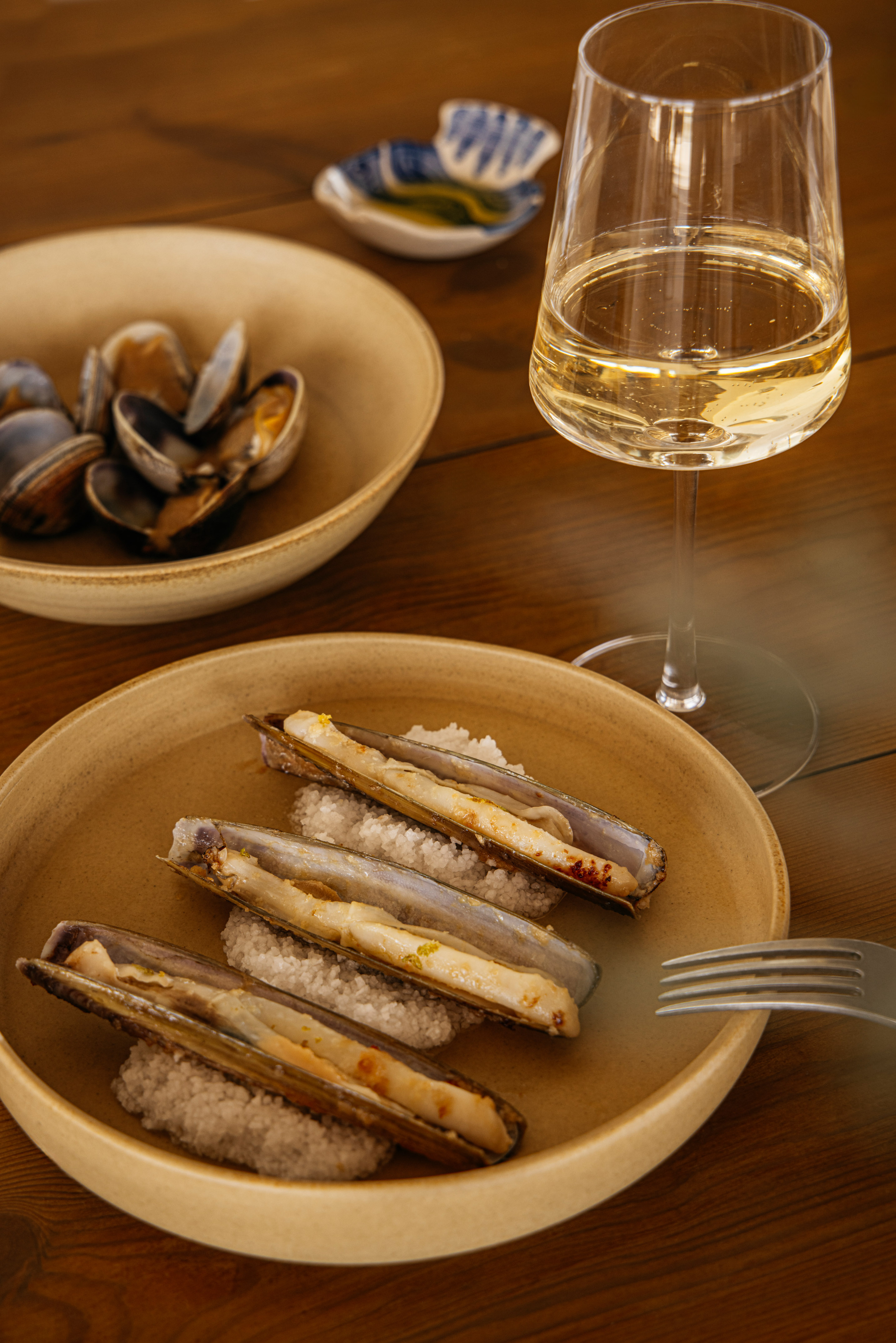 Grilled razor clams on salt, white wine, and clams on wood.