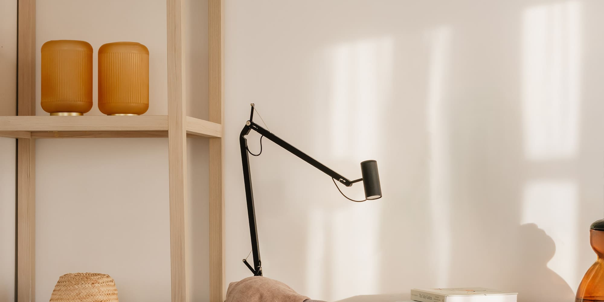 Sunlit home office with light wood desk, grey chair, black lamp, and shelf.