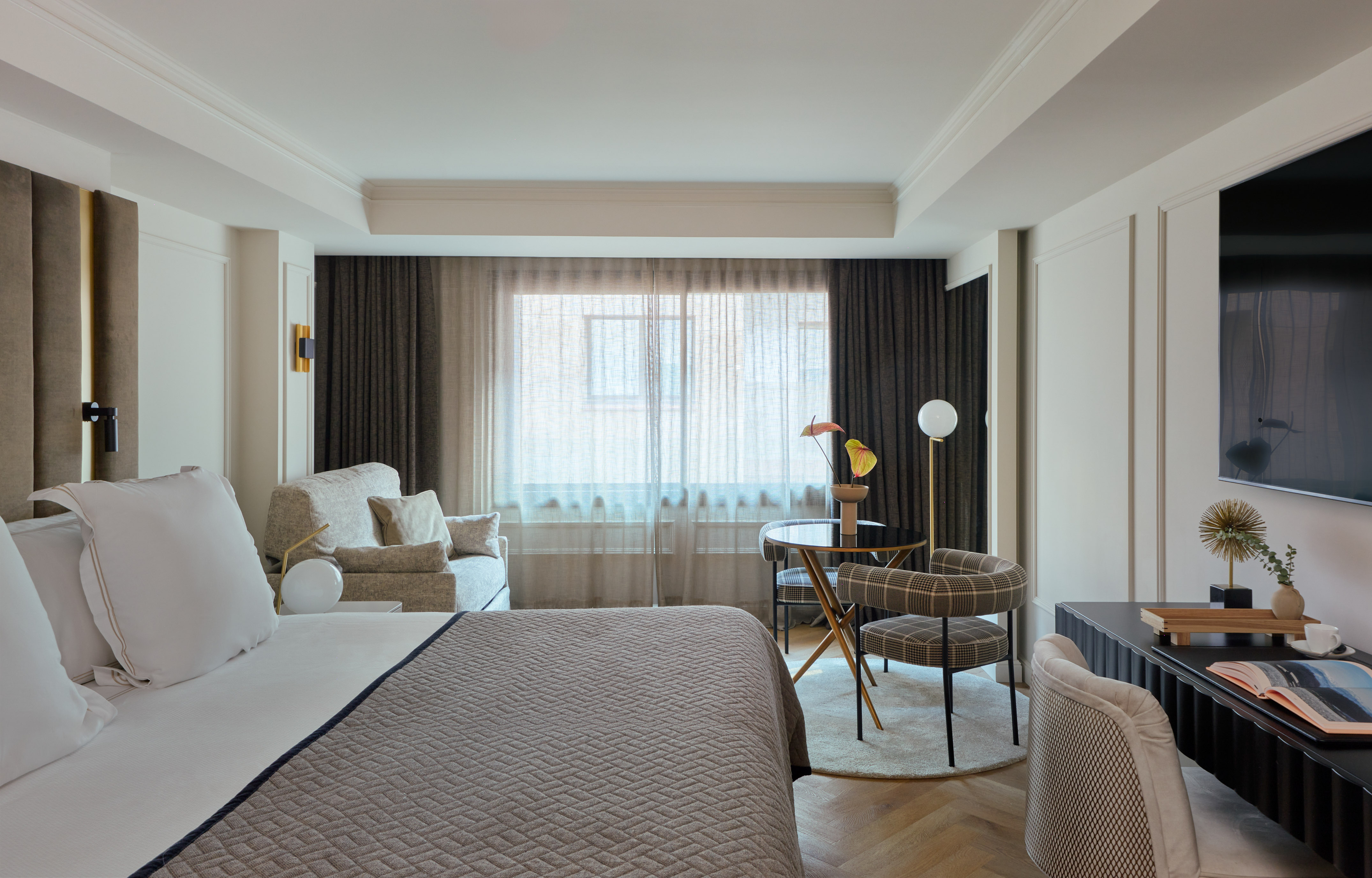 Elegant hotel room featuring a bed, lounge area, dining nook, and large window.