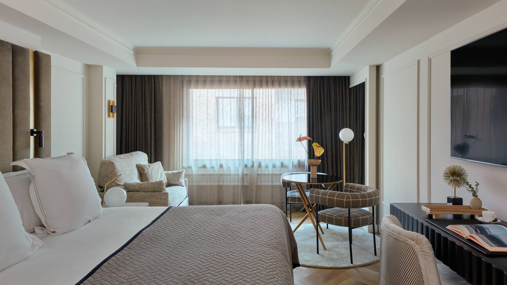 Elegant hotel room featuring a bed, lounge area, dining nook, and large window.