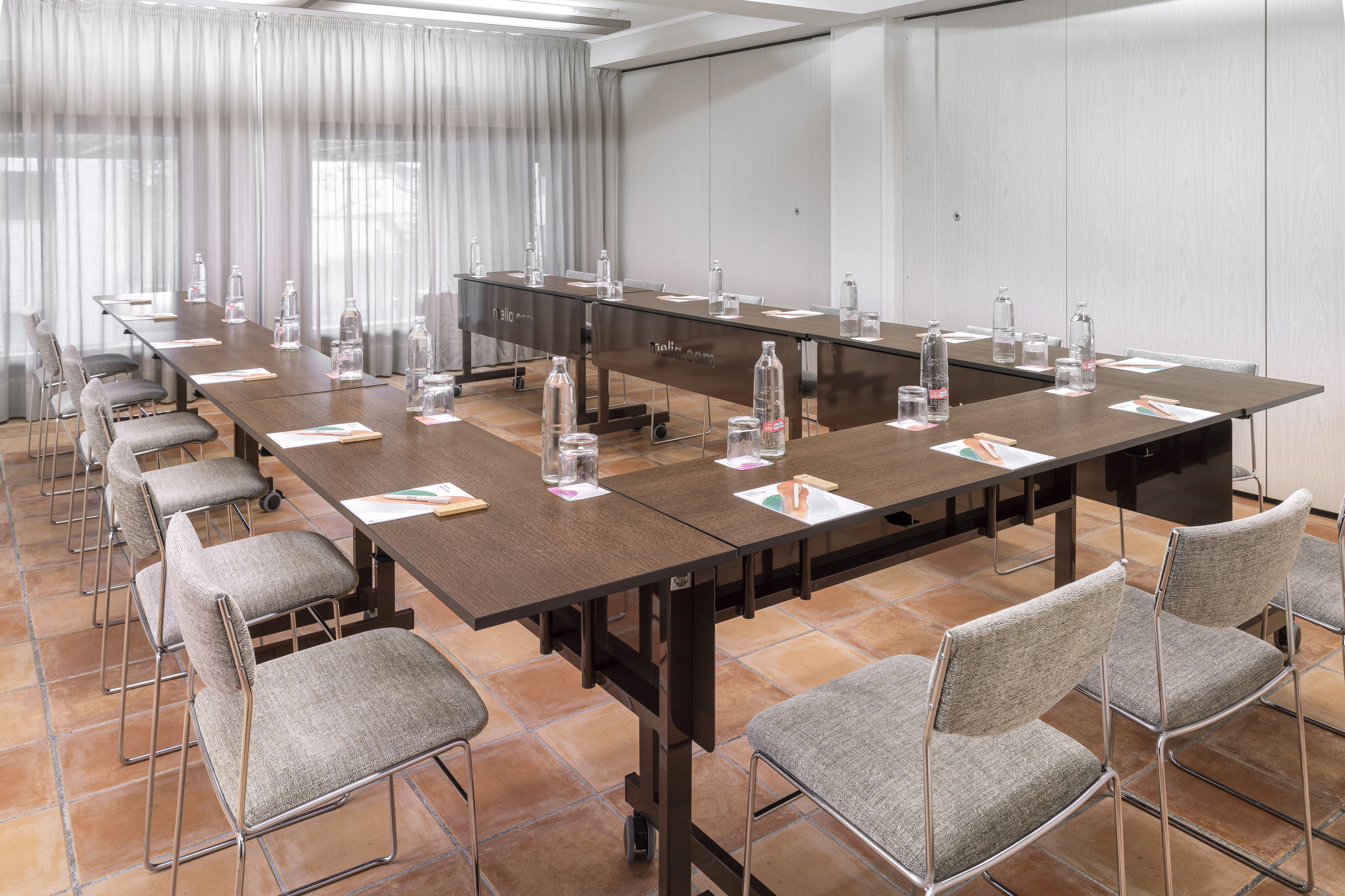 U-shaped hotel conference room with dark tables, gray chairs, and individual settings.