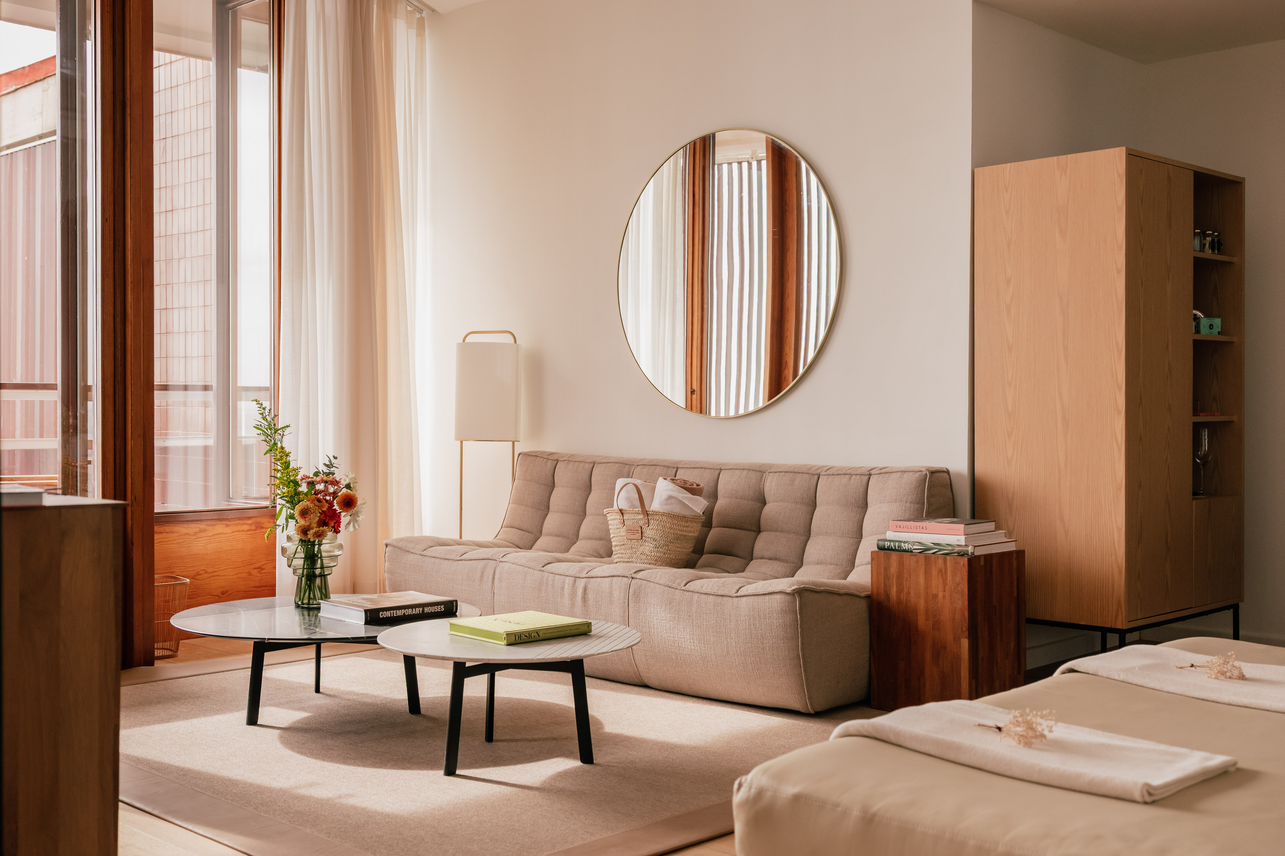 Modern living room with beige modular sofa, round mirror, and coffee tables.