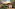 Couple walks towards a luxury glamping tent on a wooden deck in a forest.