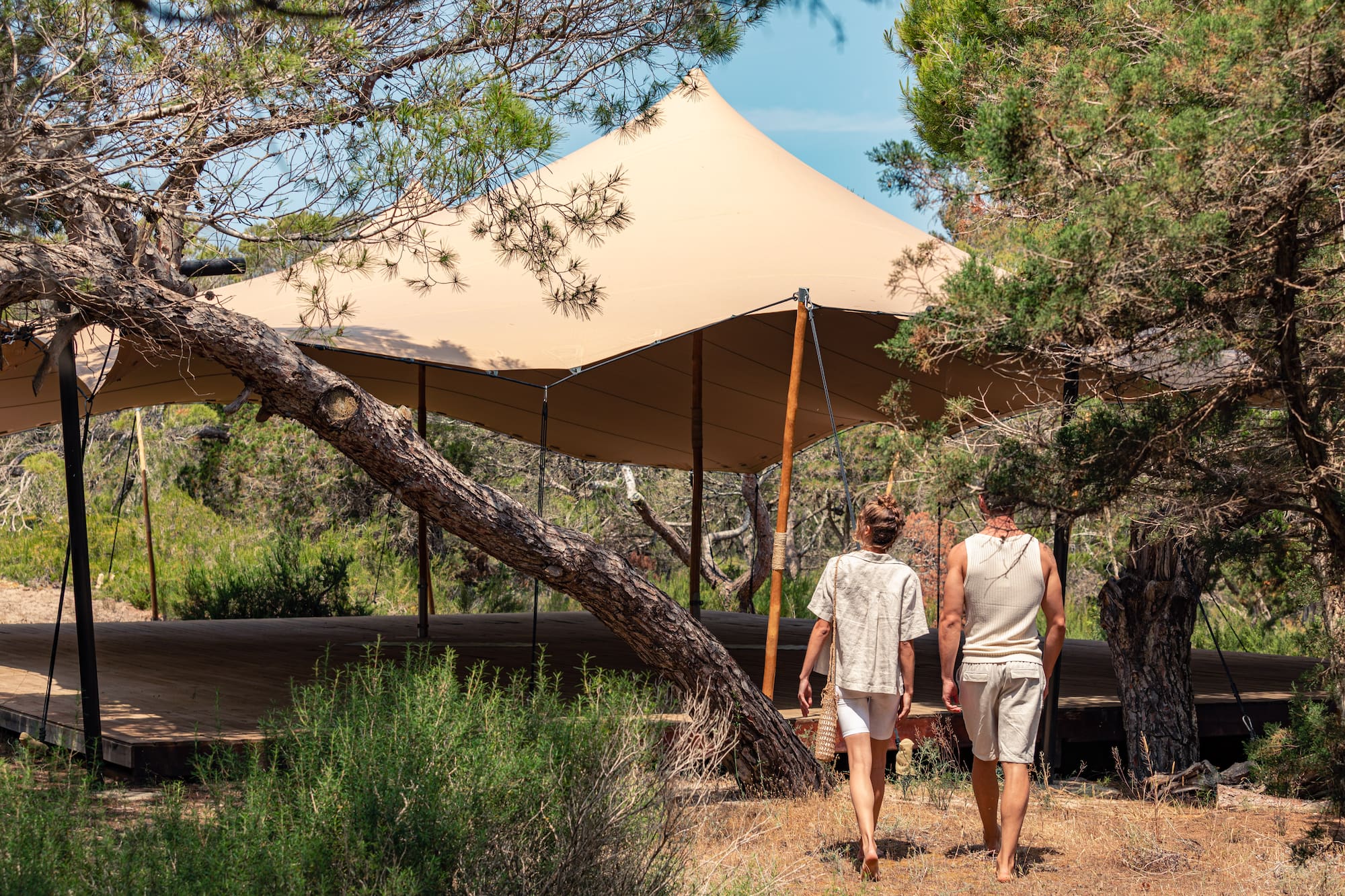 Couple walks towards a luxury glamping tent on a wooden deck in a forest.