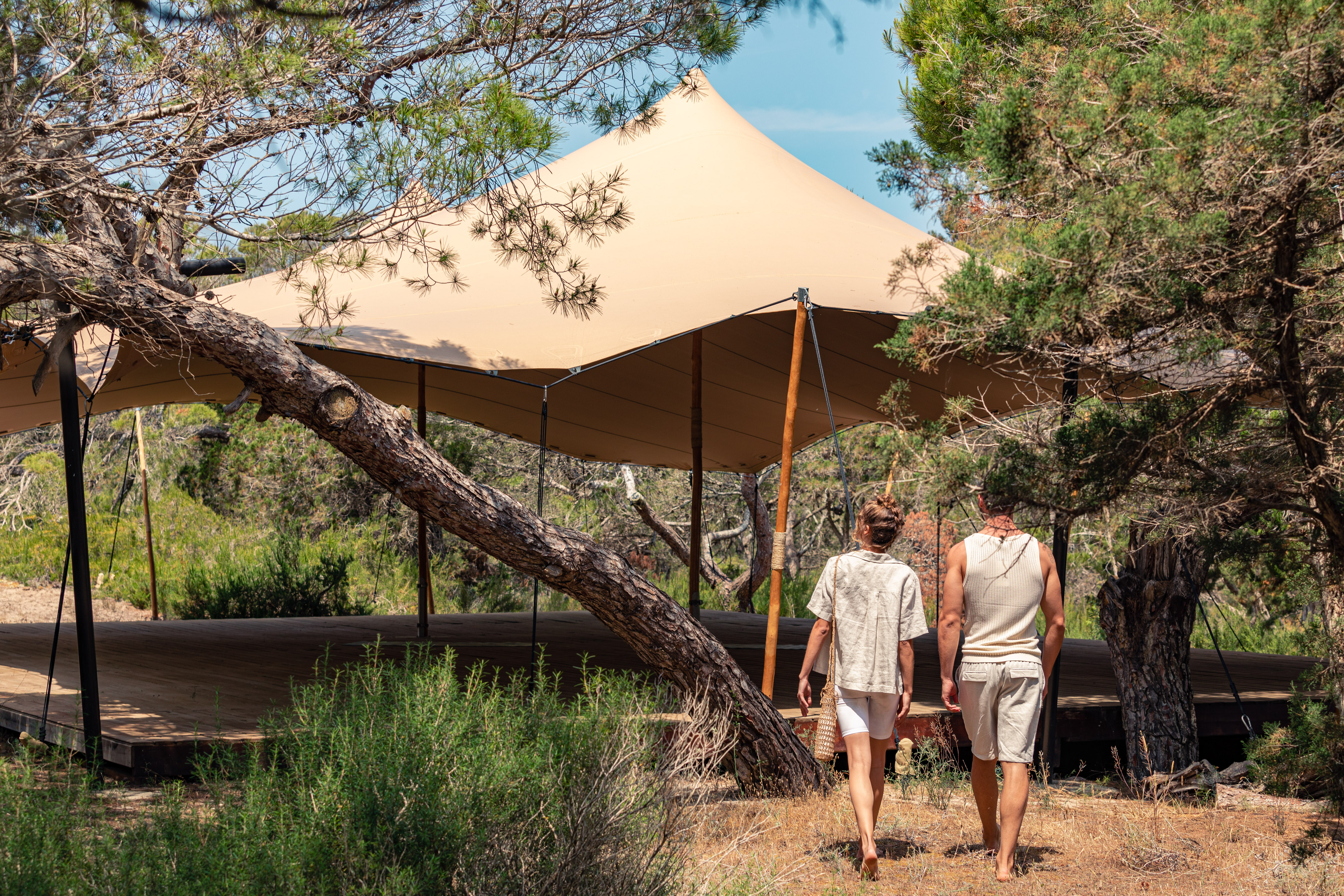 Couple walks towards a luxury glamping tent on a wooden deck in a forest.