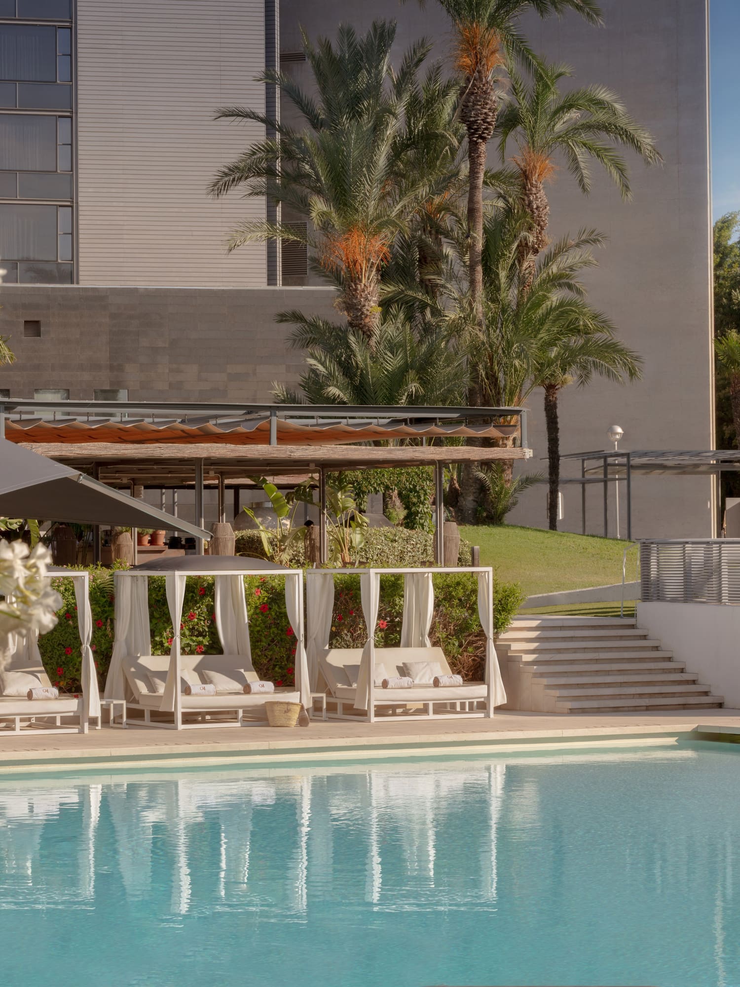 Luxury resort pool with white cabanas, palm trees, and modern hotel.