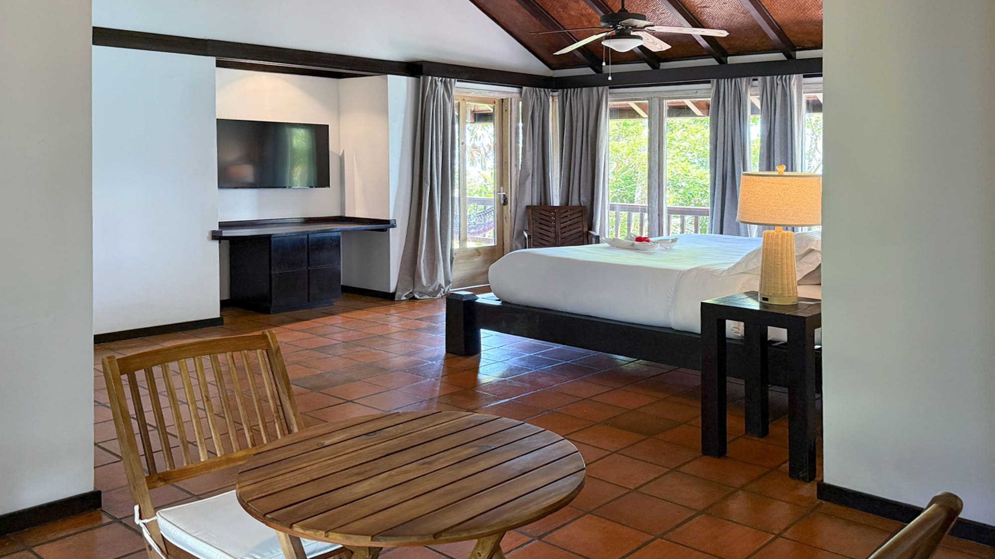 Cozy resort bedroom with king bed, vaulted wood ceiling, balcony, and tile floor.