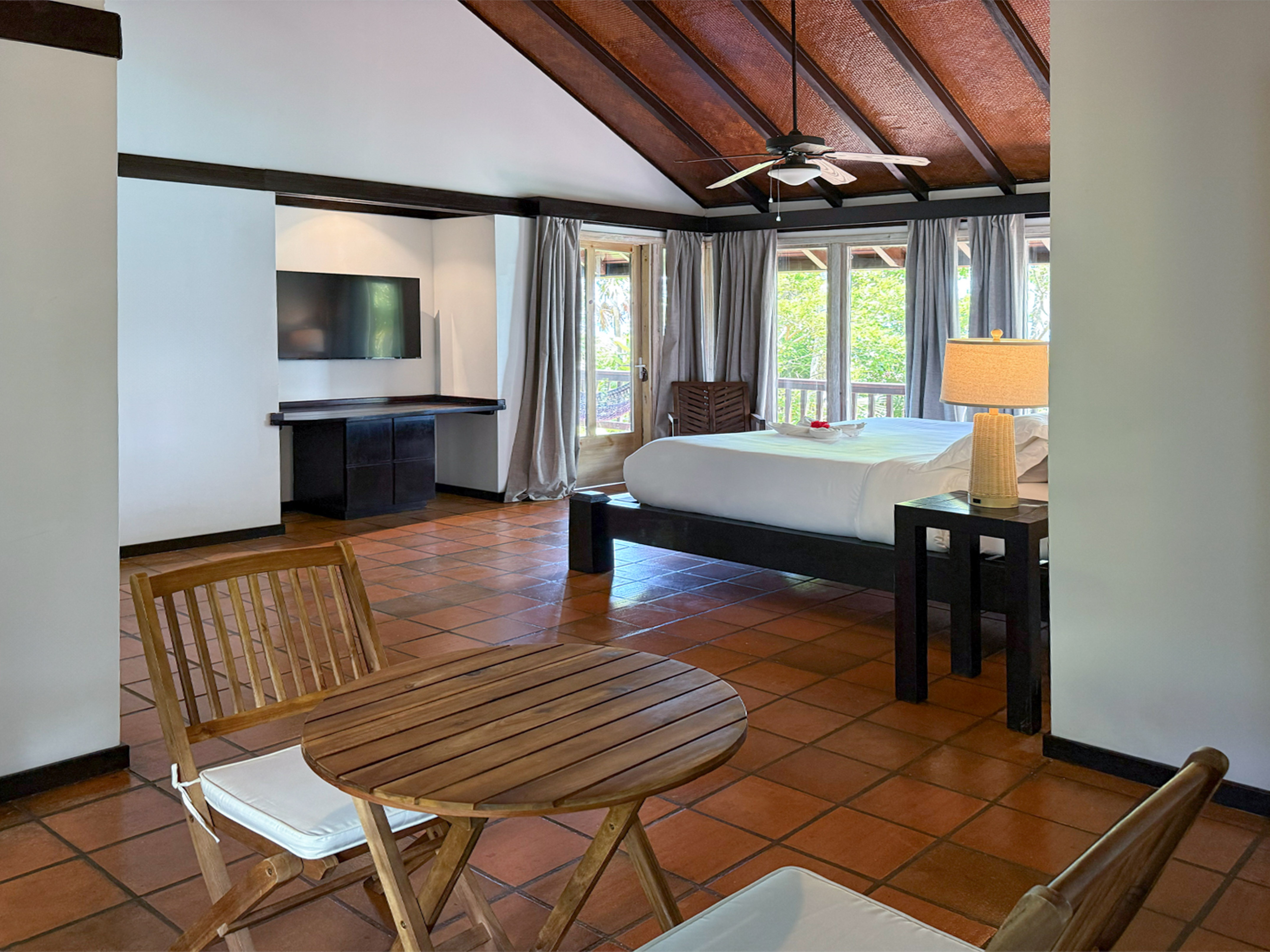 Cozy resort bedroom with king bed, vaulted wood ceiling, balcony, and tile floor.