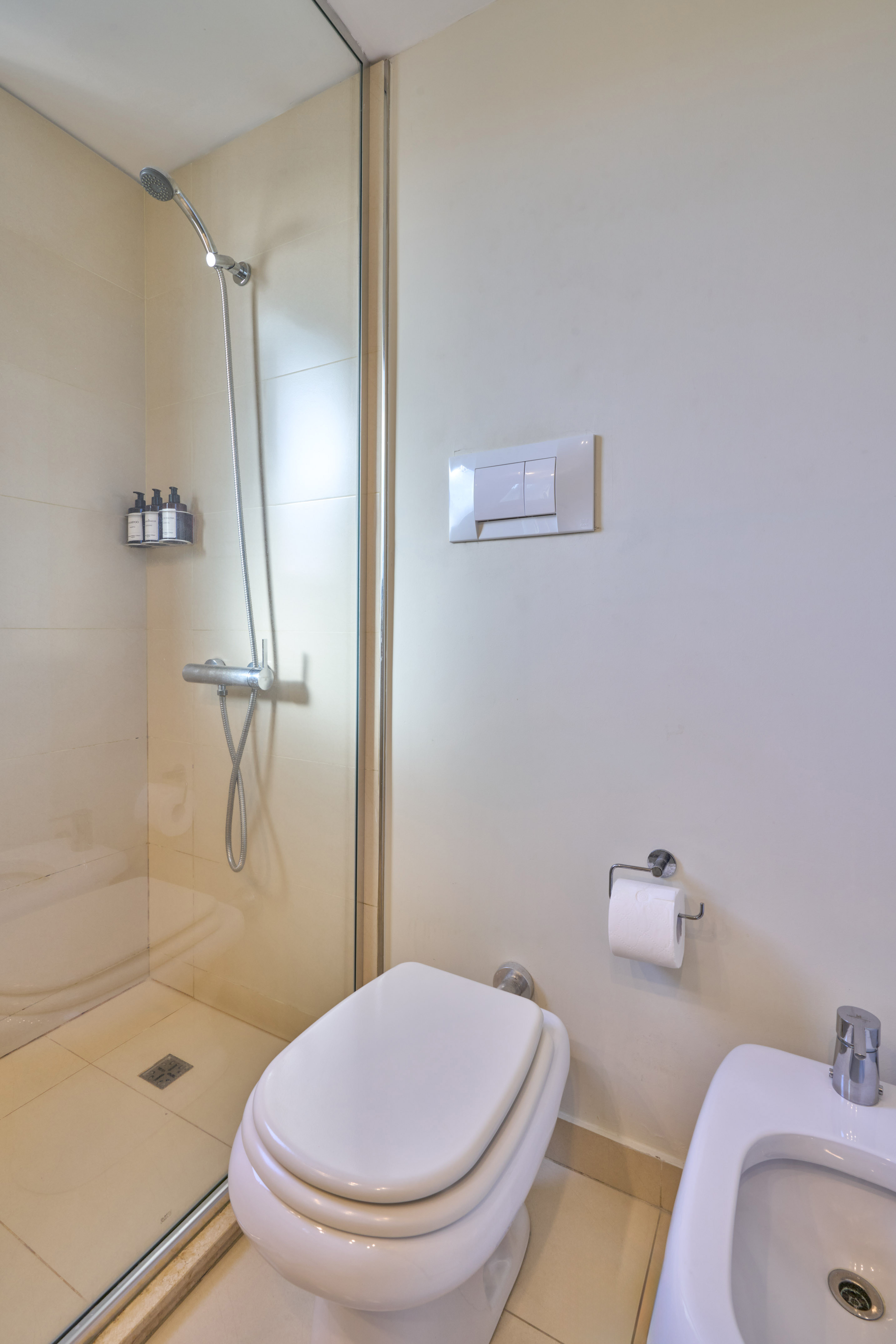 Clean bathroom interior with glass shower, toilet, and bidet.