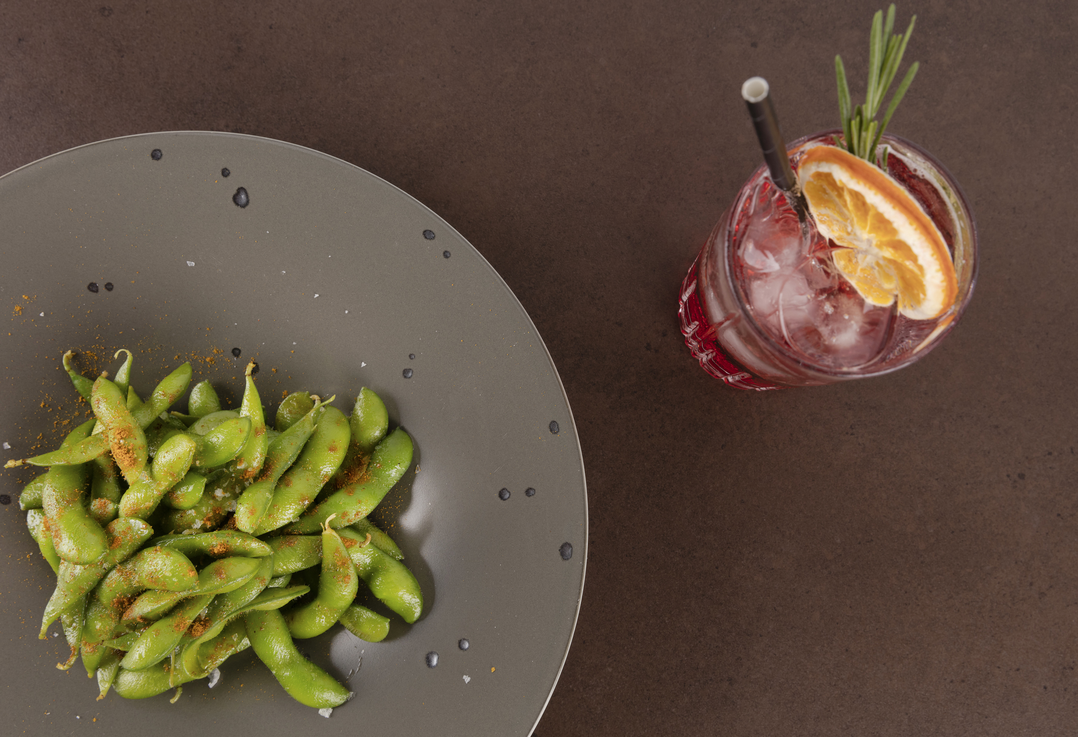 Spiced edamame on plate, red cocktail with orange and rosemary.