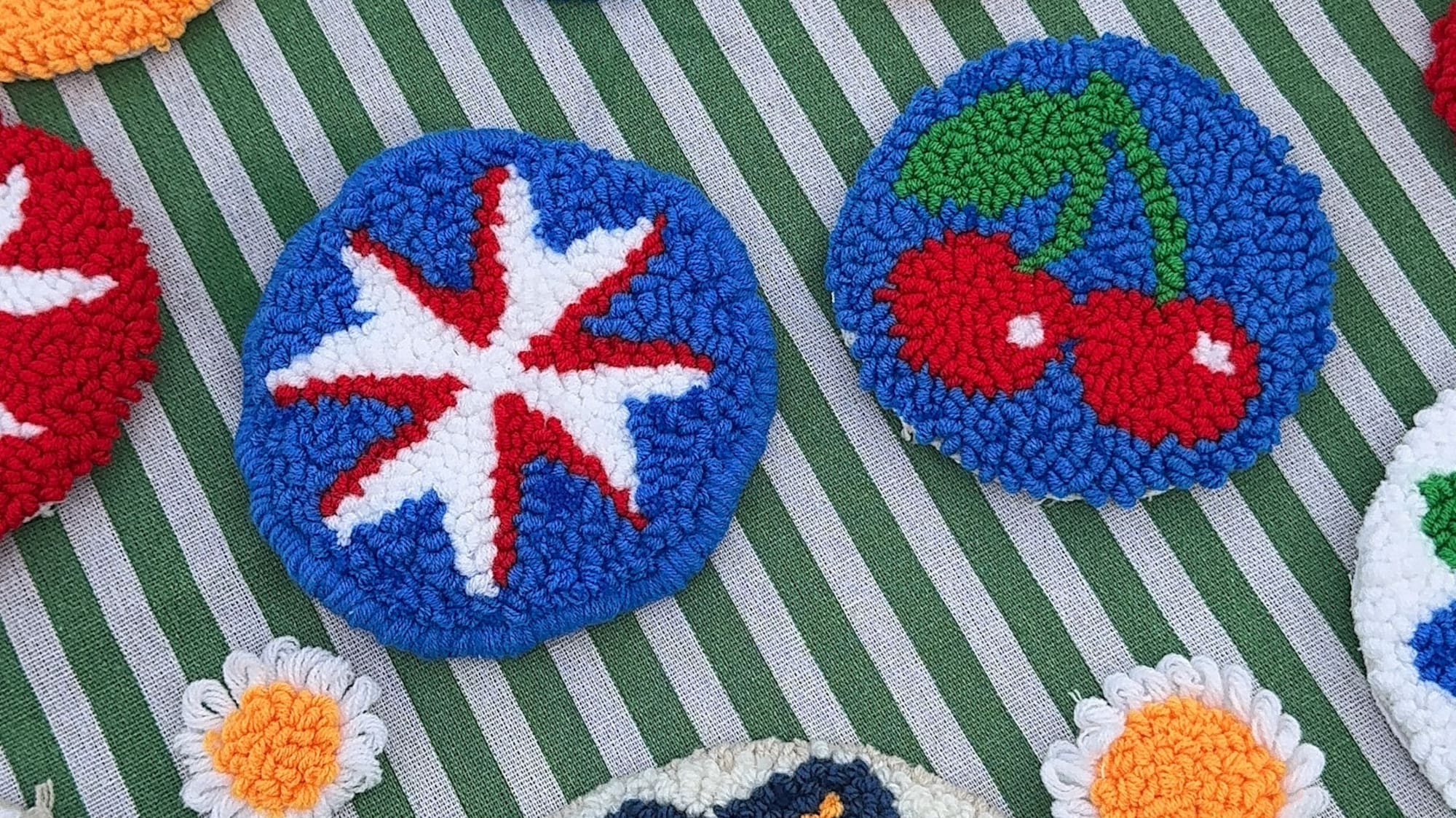 Colorful punch needle coasters with diverse patterns on green striped fabric.