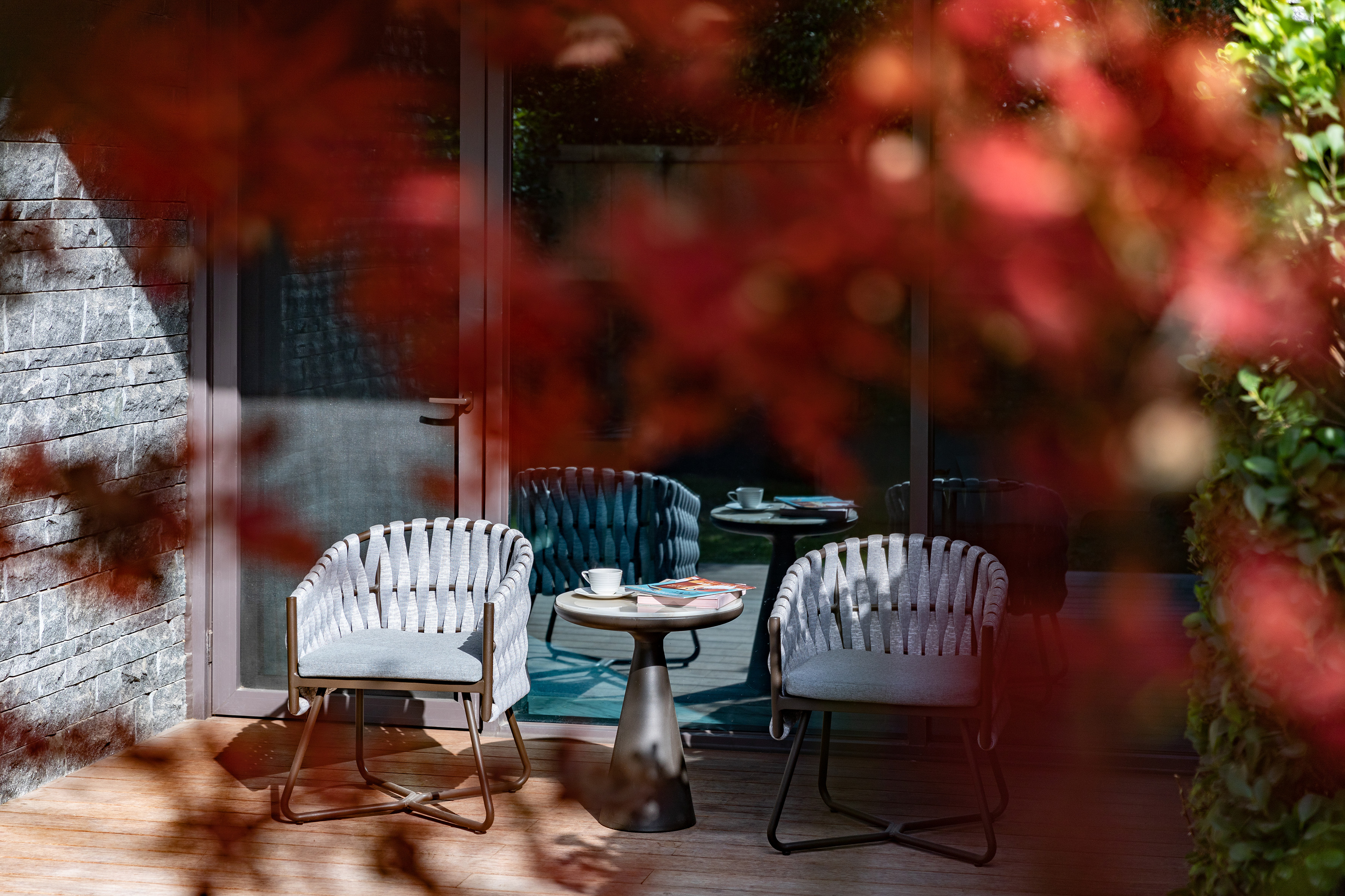 Two woven outdoor chairs and table on wooden deck, red autumn leaves.