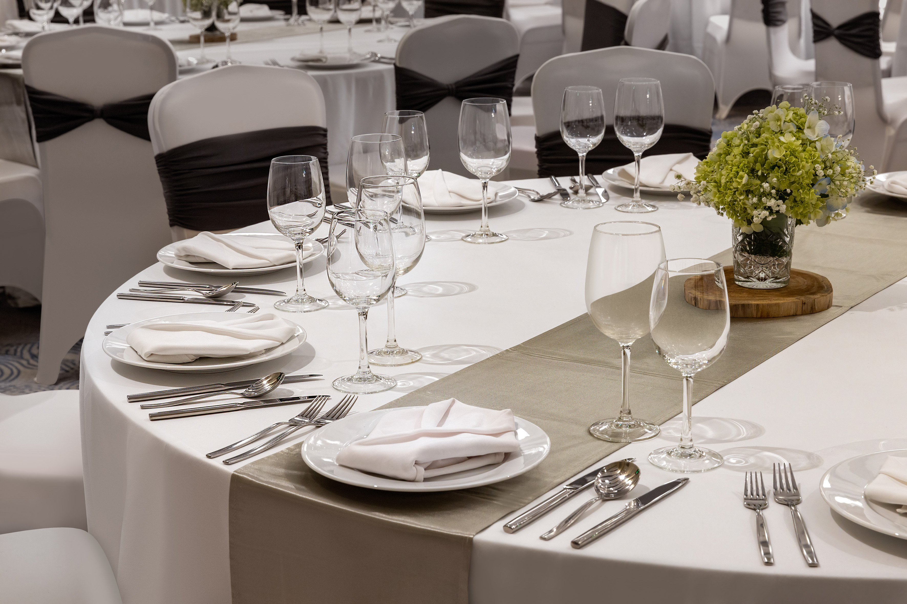 Formal dining table with white place settings, glasses, and green floral centerpiece.