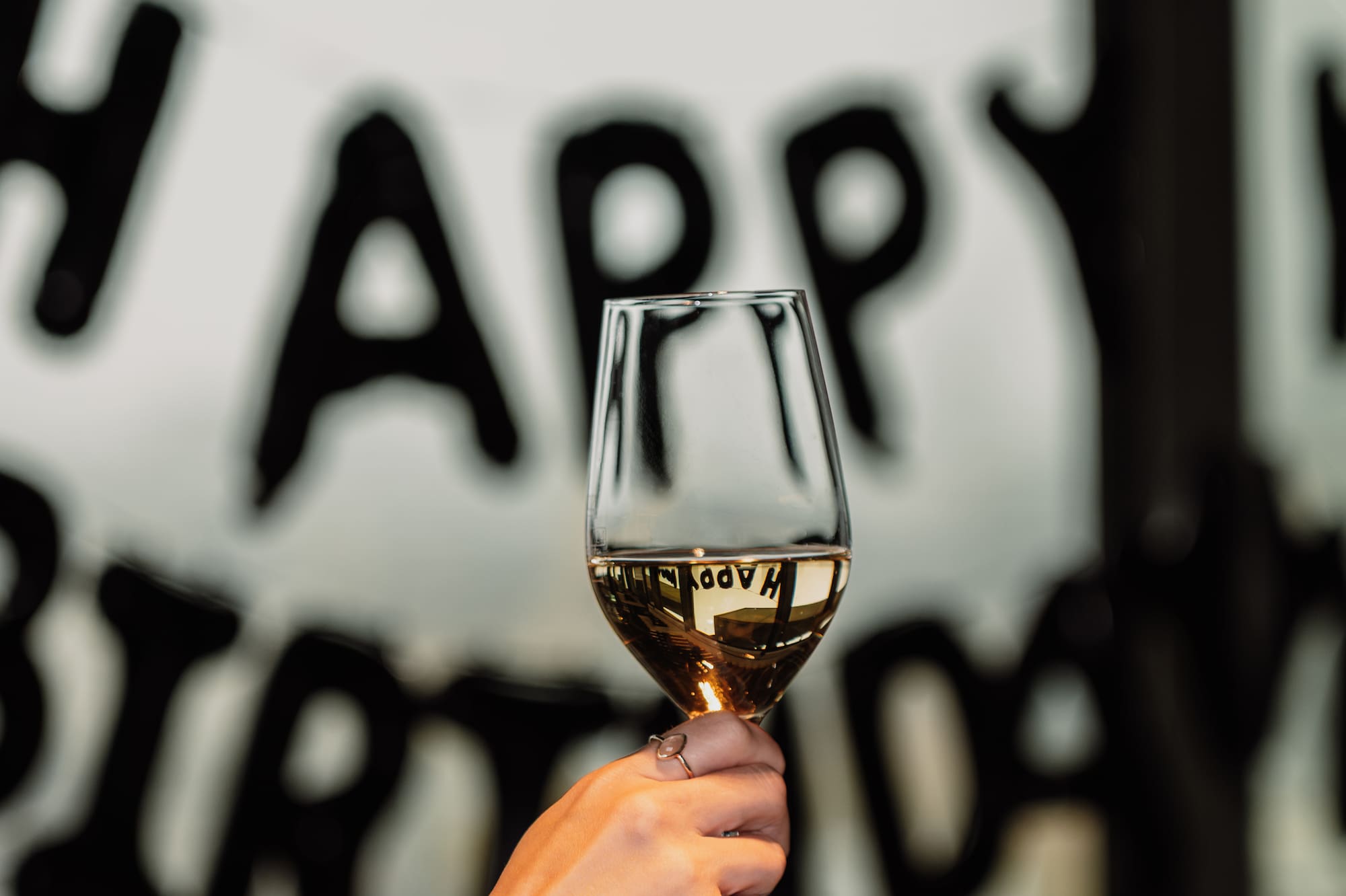 Toasting with white wine glass, reflection of "Happy Birthday" banner.