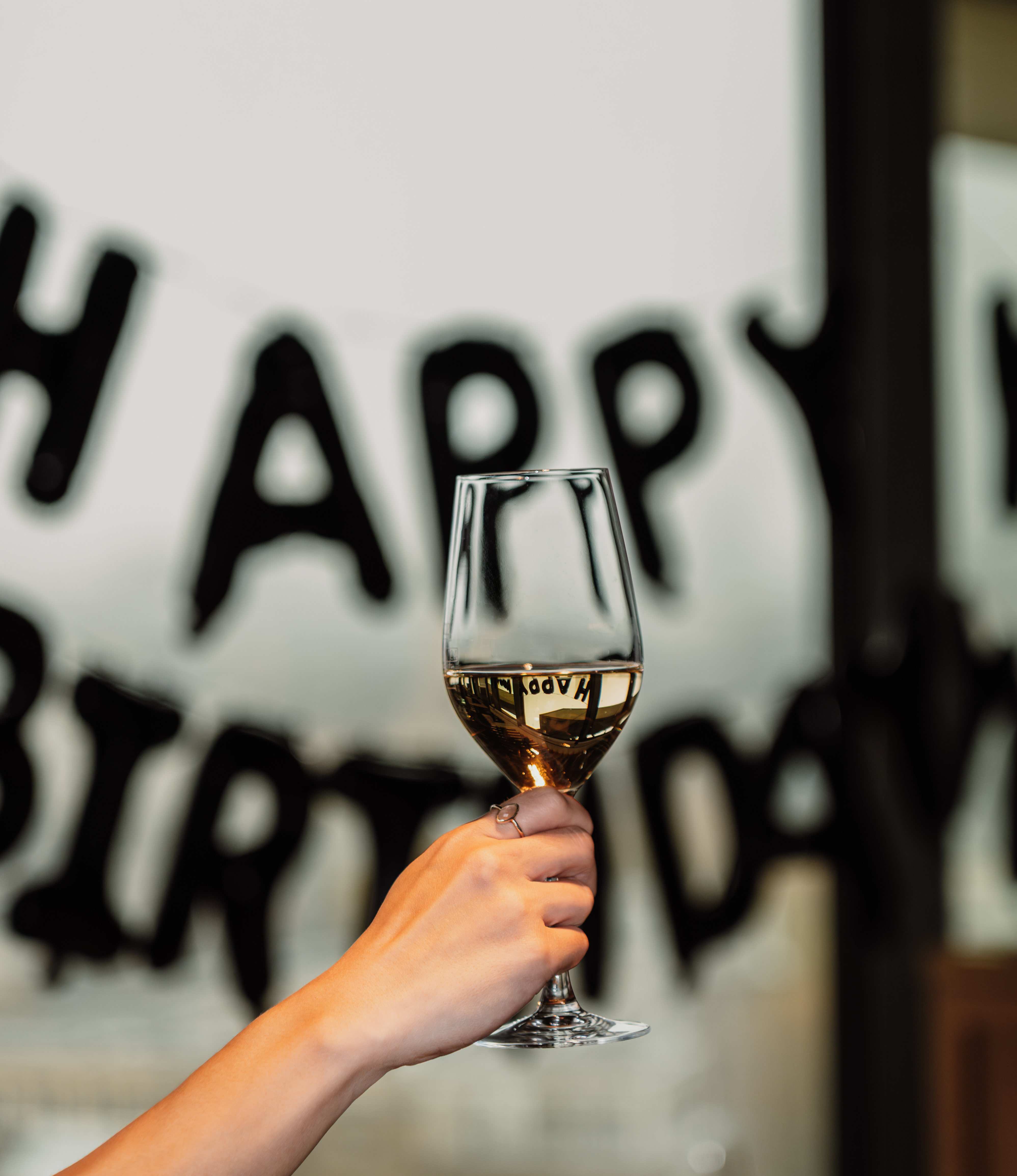 Toasting with white wine glass, reflection of "Happy Birthday" banner.
