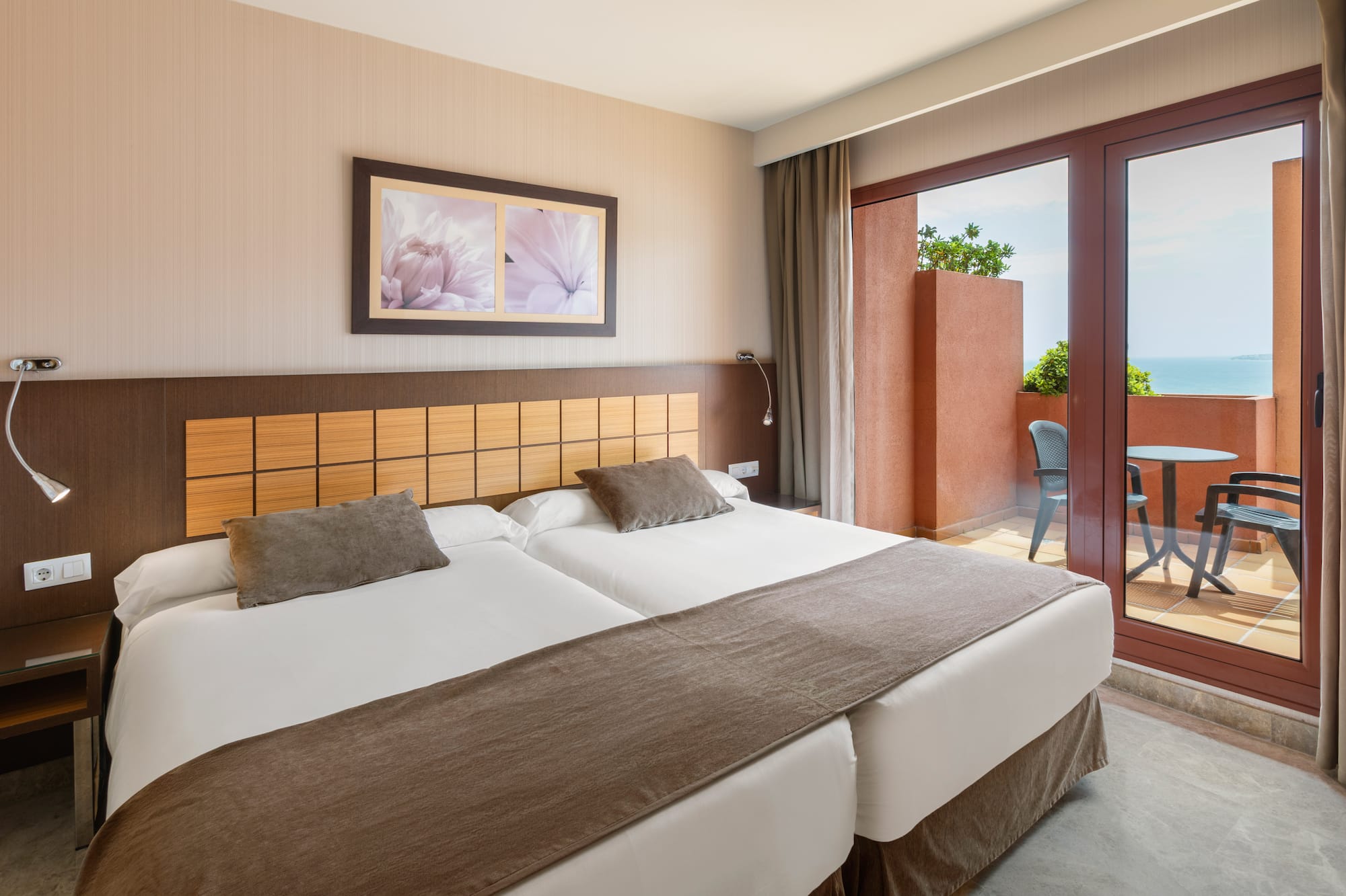 Modern hotel room with twin beds, balcony, and sea view.