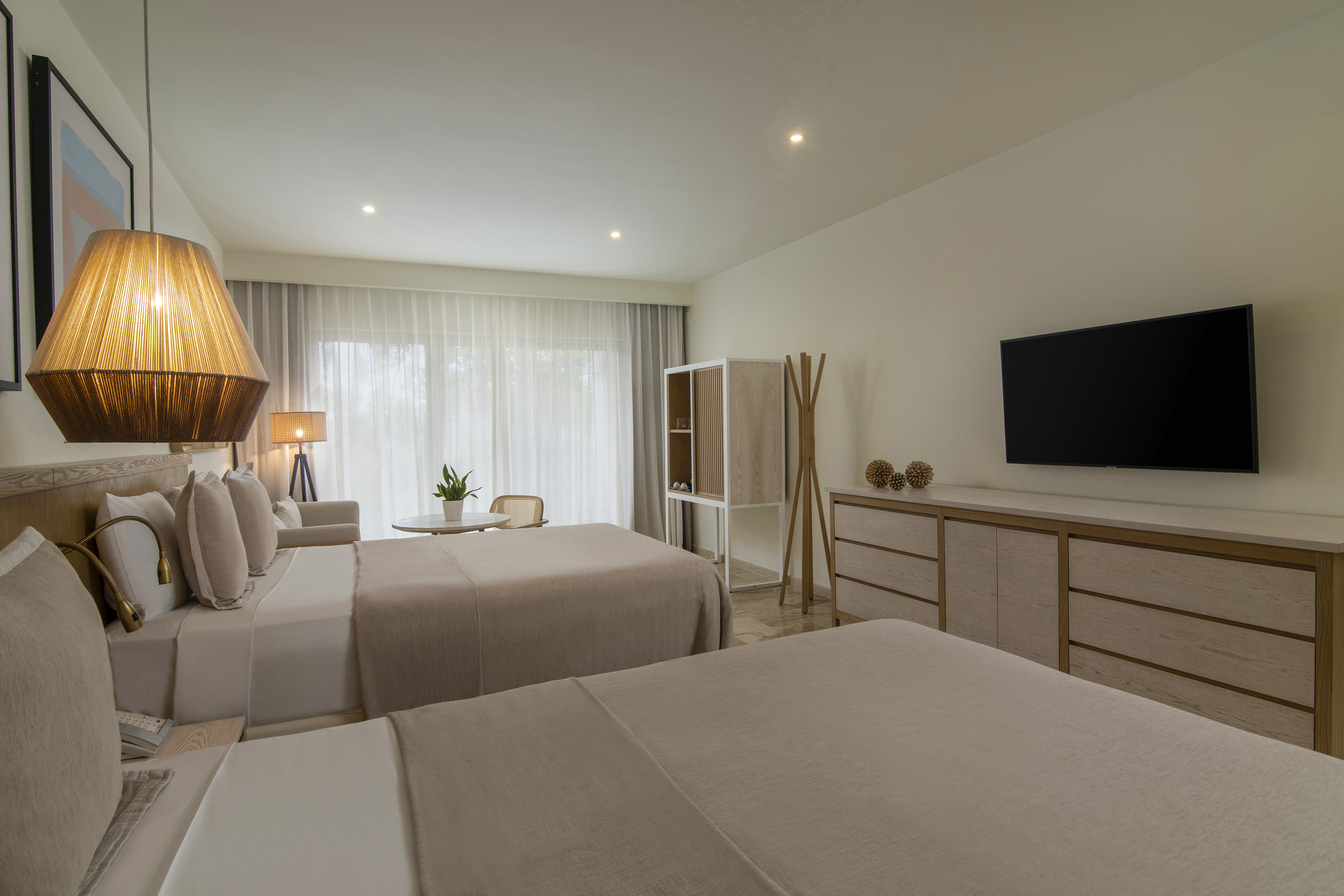 Modern hotel room with two beds, neutral decor, TV, and bright window.