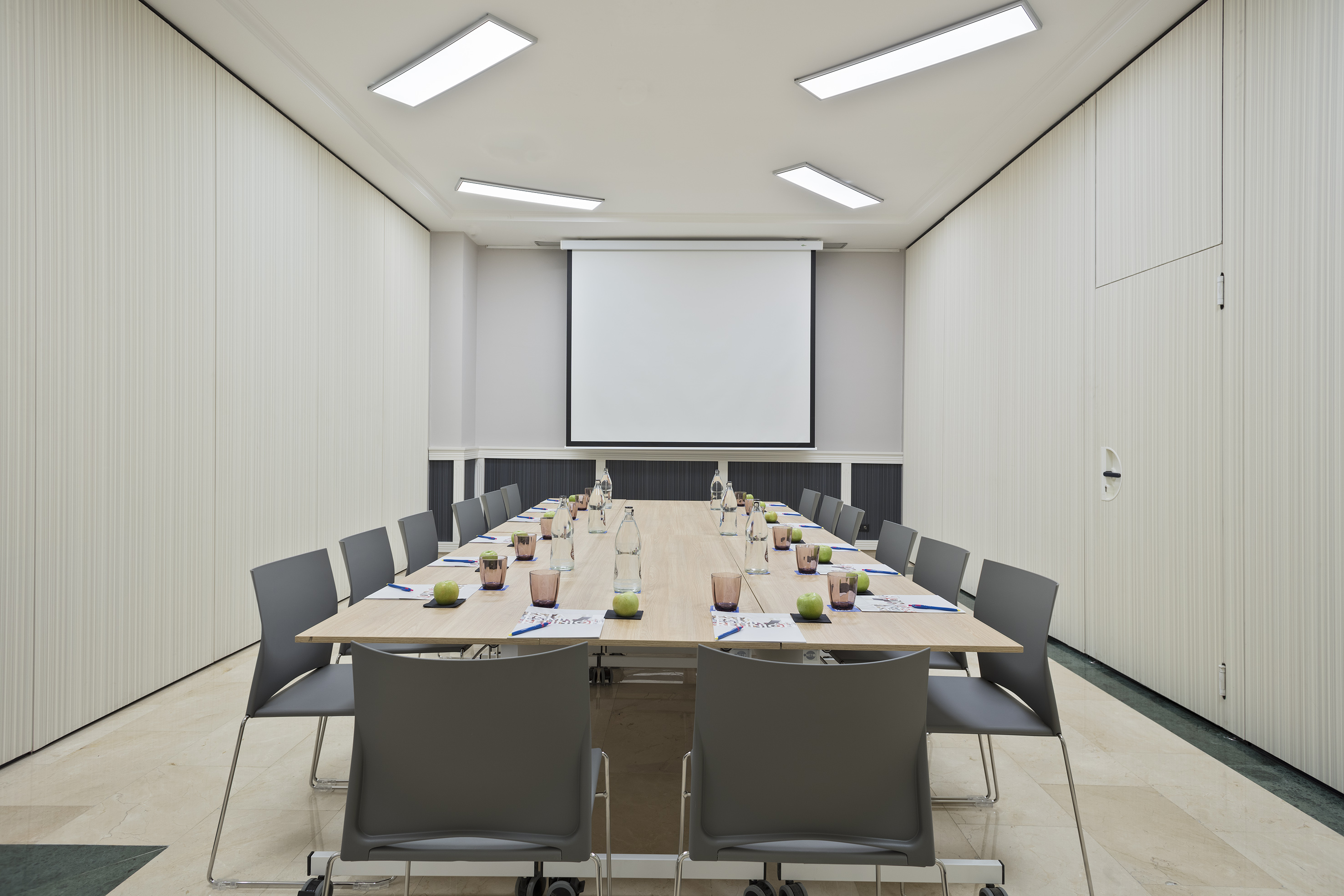 Modern conference room with large table, chairs, and projector screen.