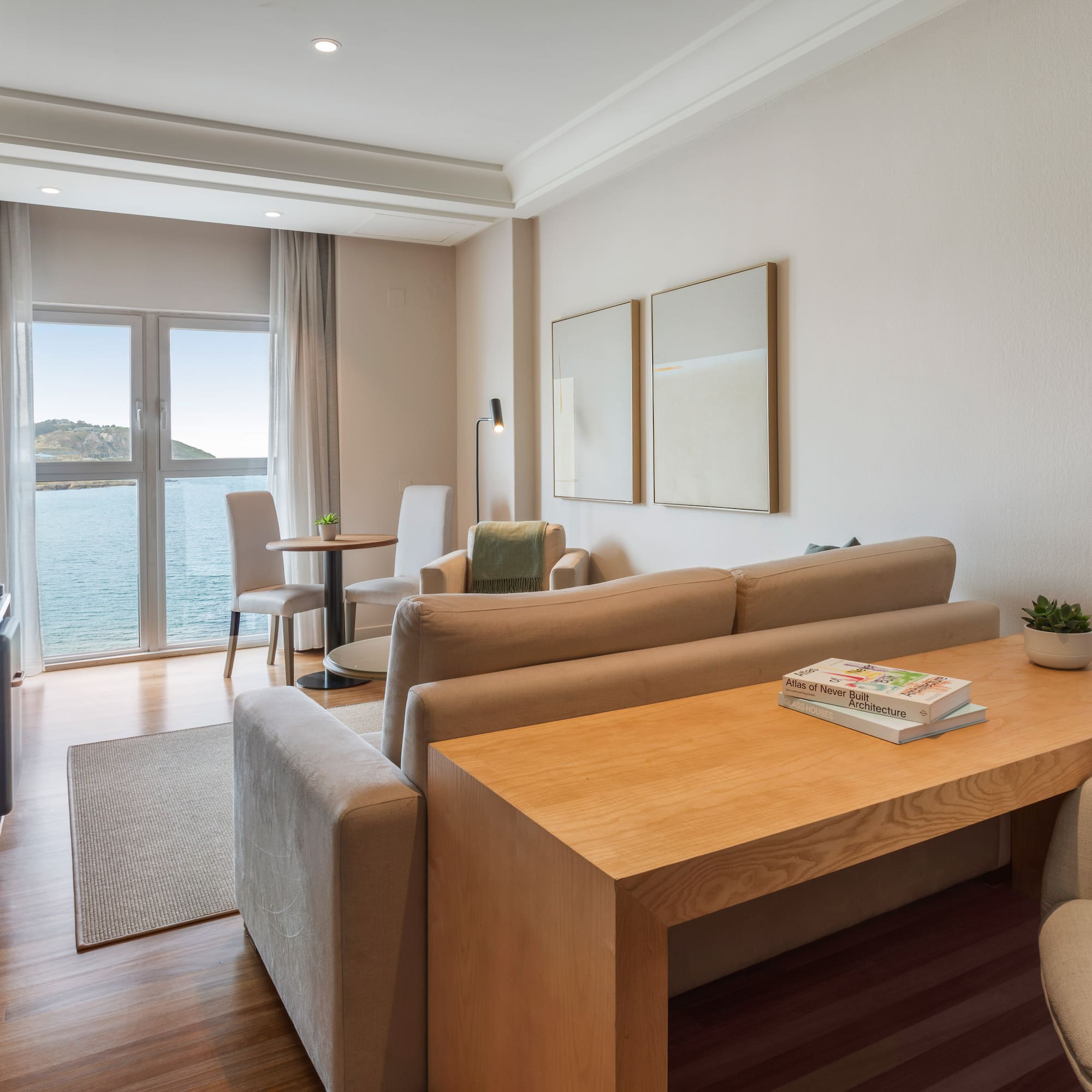 Salón de suite con vistas al mar, sofá beige, mesa de centro y TV.