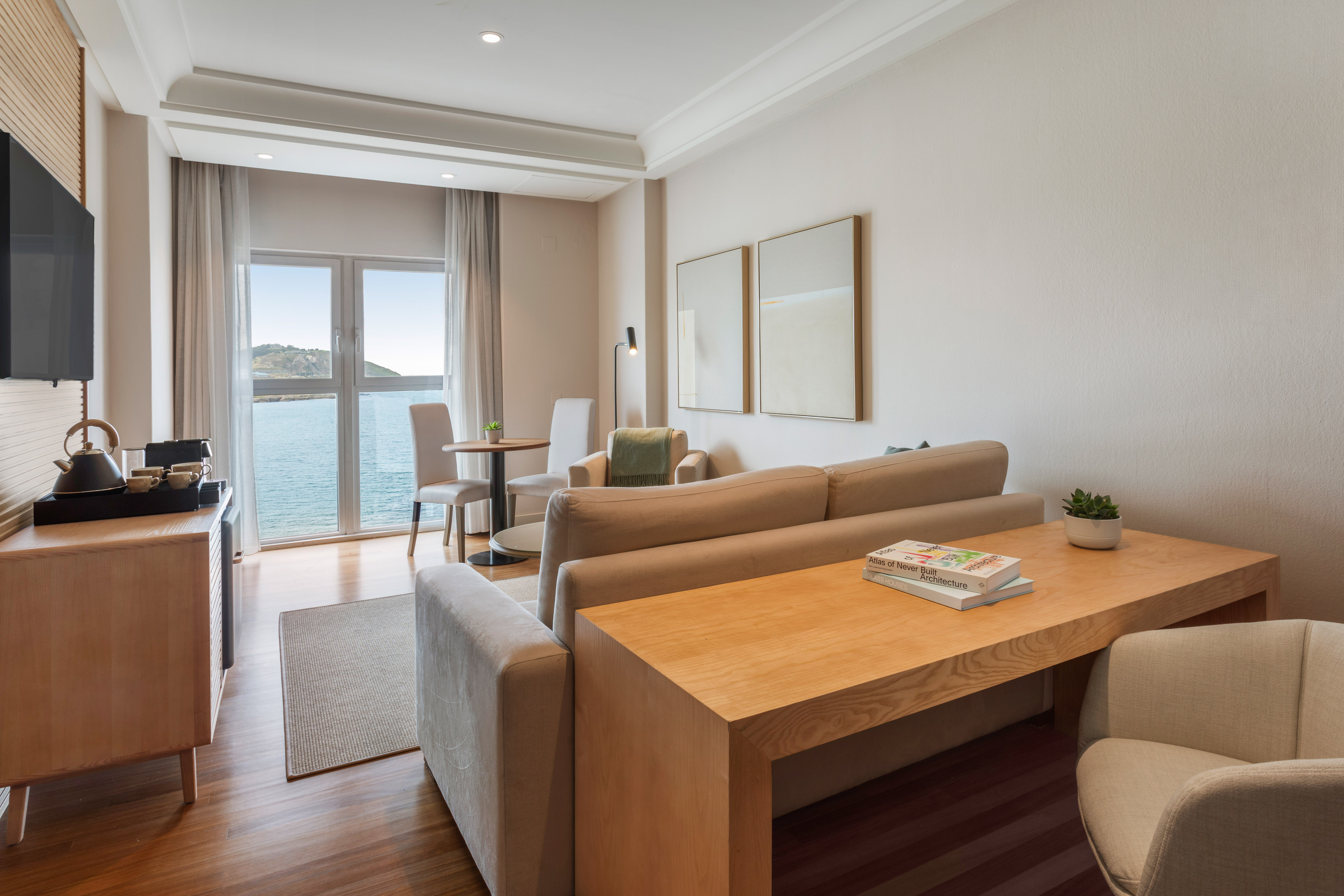 Salón de suite con vistas al mar, sofá beige, mesa de centro y TV.