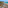 Balcony with table & chairs overlooking turquoise sea, sandy beach, and rocky coast.