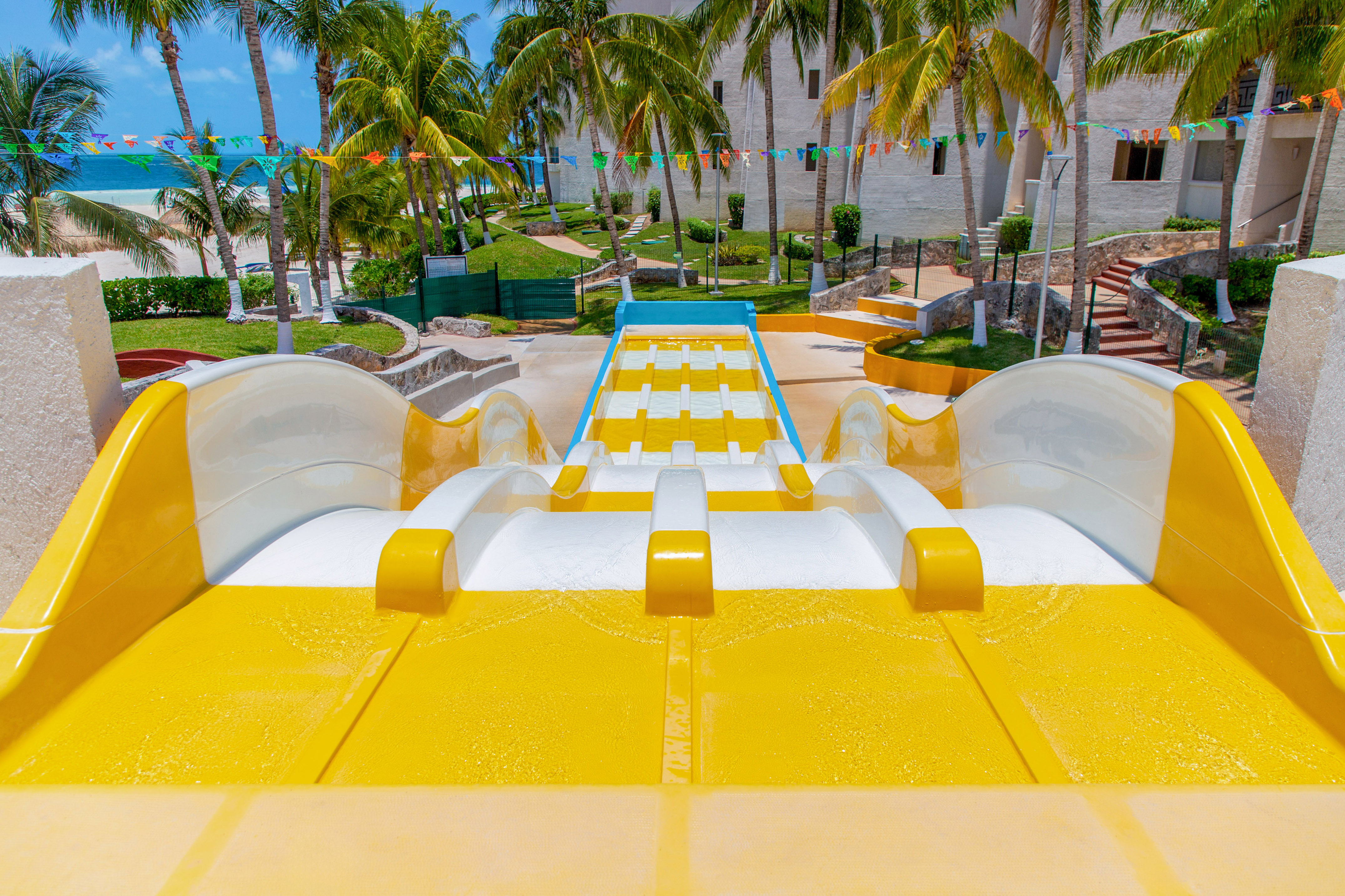 Yellow and white multi-lane water slide at a tropical beach resort with palm trees.