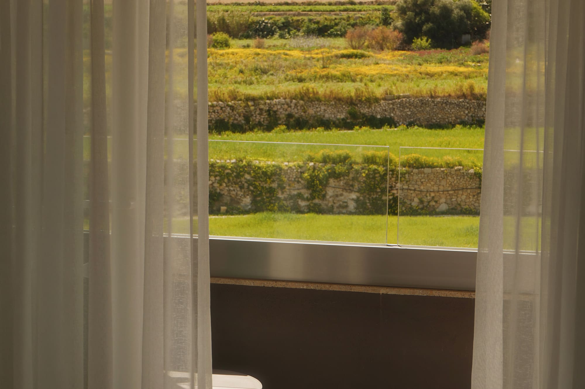 Bedroom view: terraced hills, hill-top statue, sheer curtains, open book, mug.