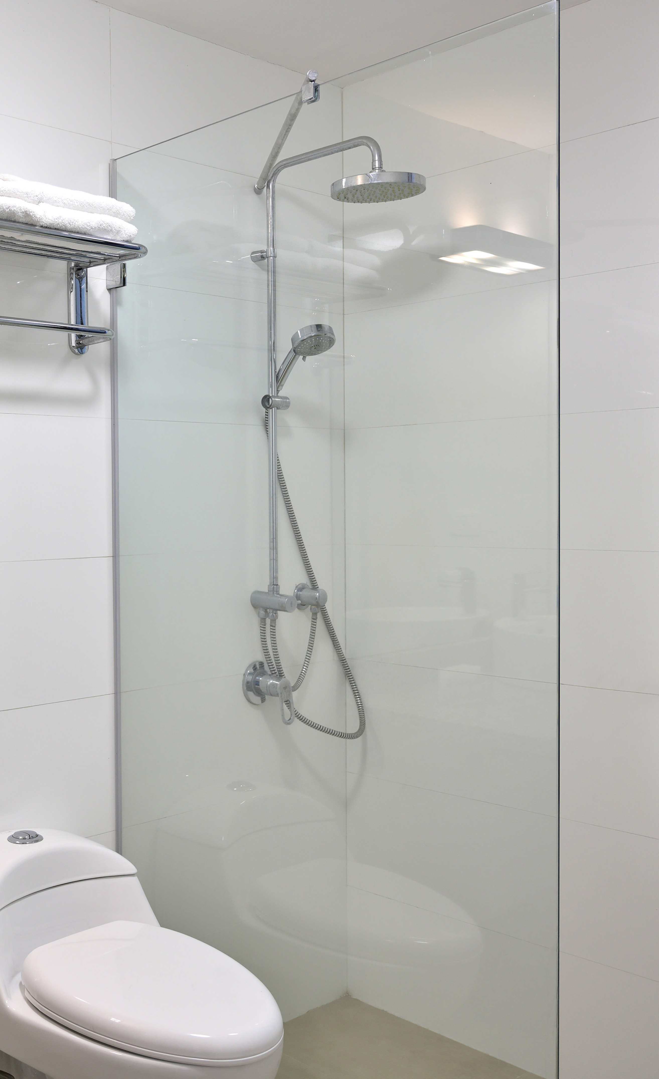 Modern white bathroom with glass shower enclosure, chrome fixtures, and toilet.