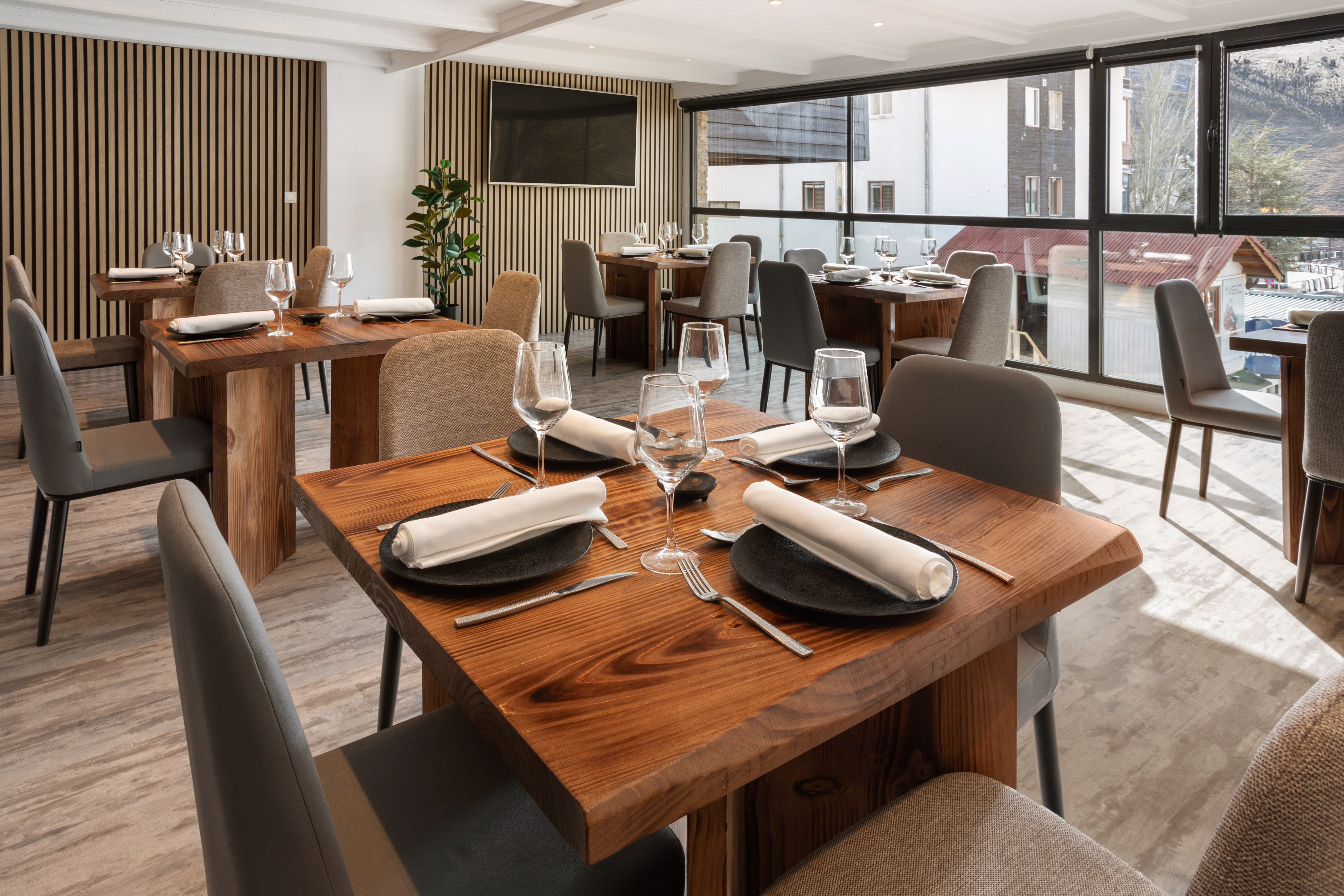 Modern restaurant dining room with wooden tables, grey chairs, and a window view.