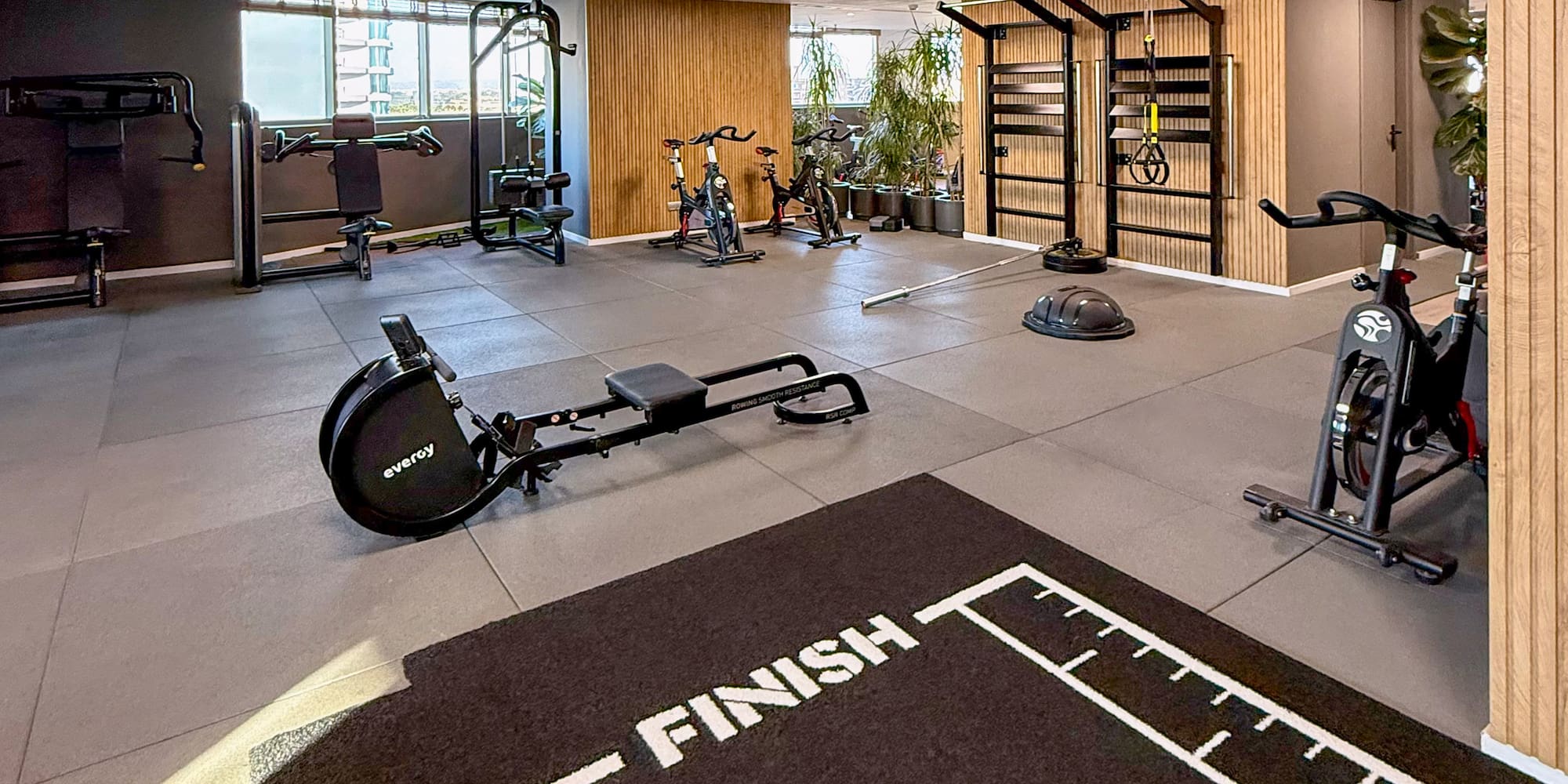 Modern gym with rowing machine, exercise bikes, weight machines, and a FINISH mat.