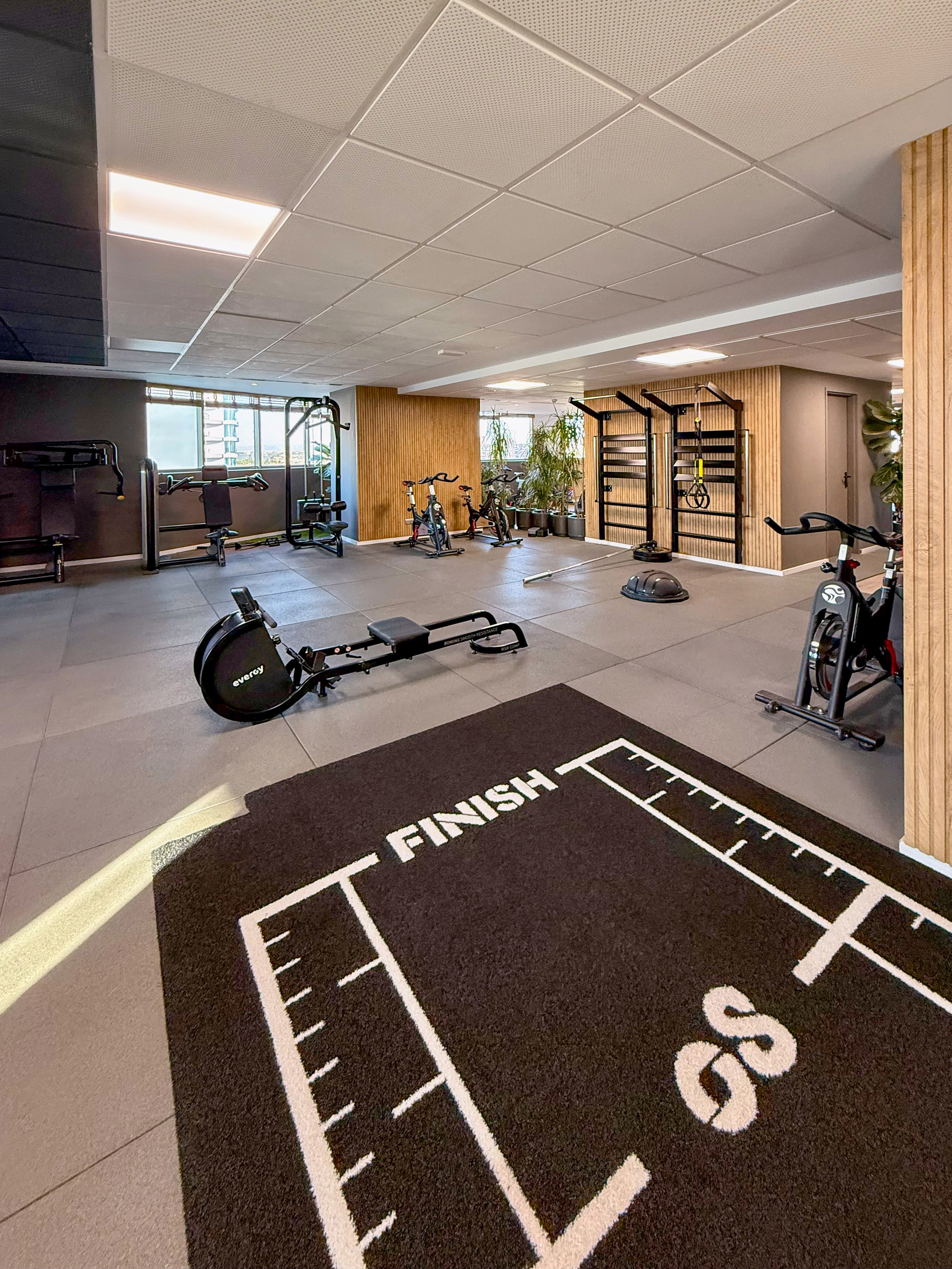 Modern gym with rowing machine, exercise bikes, weight machines, and a FINISH mat.