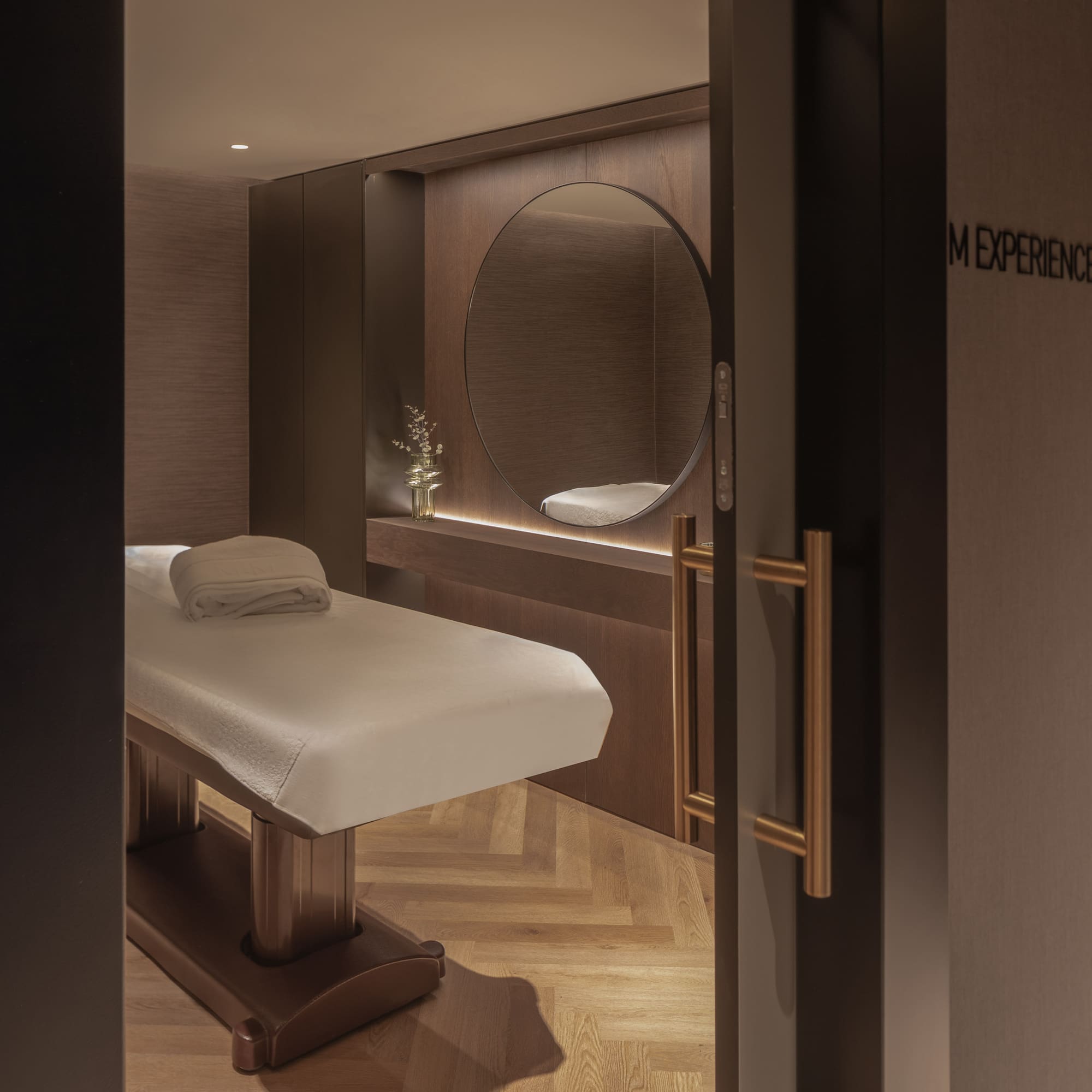 Luxury spa treatment room with massage table, circular mirror, and warm lighting.