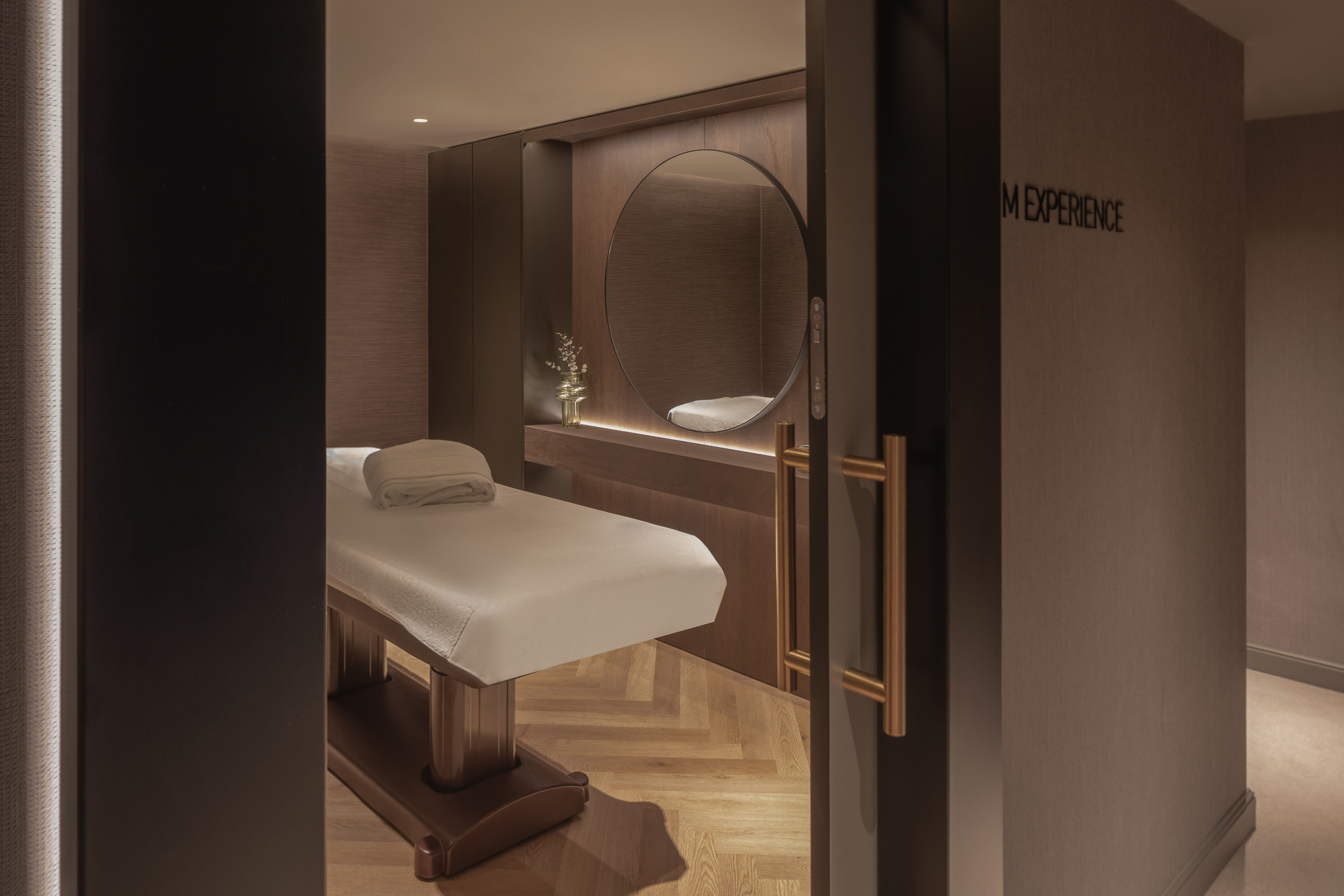 Luxury spa treatment room with massage table, circular mirror, and warm lighting.