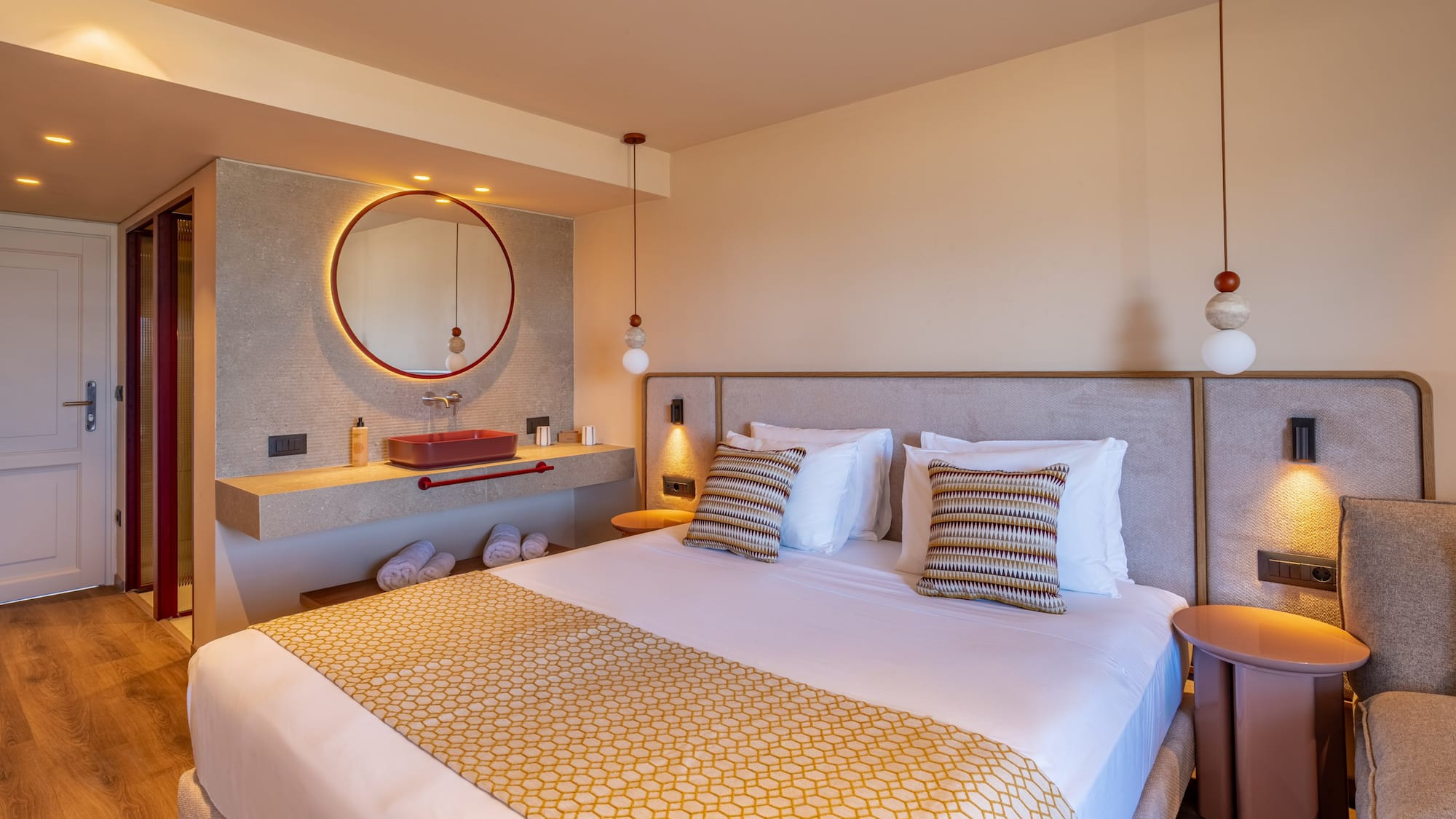 Luxurious modern hotel room with king bed, red vanity sink, and round backlit mirror.