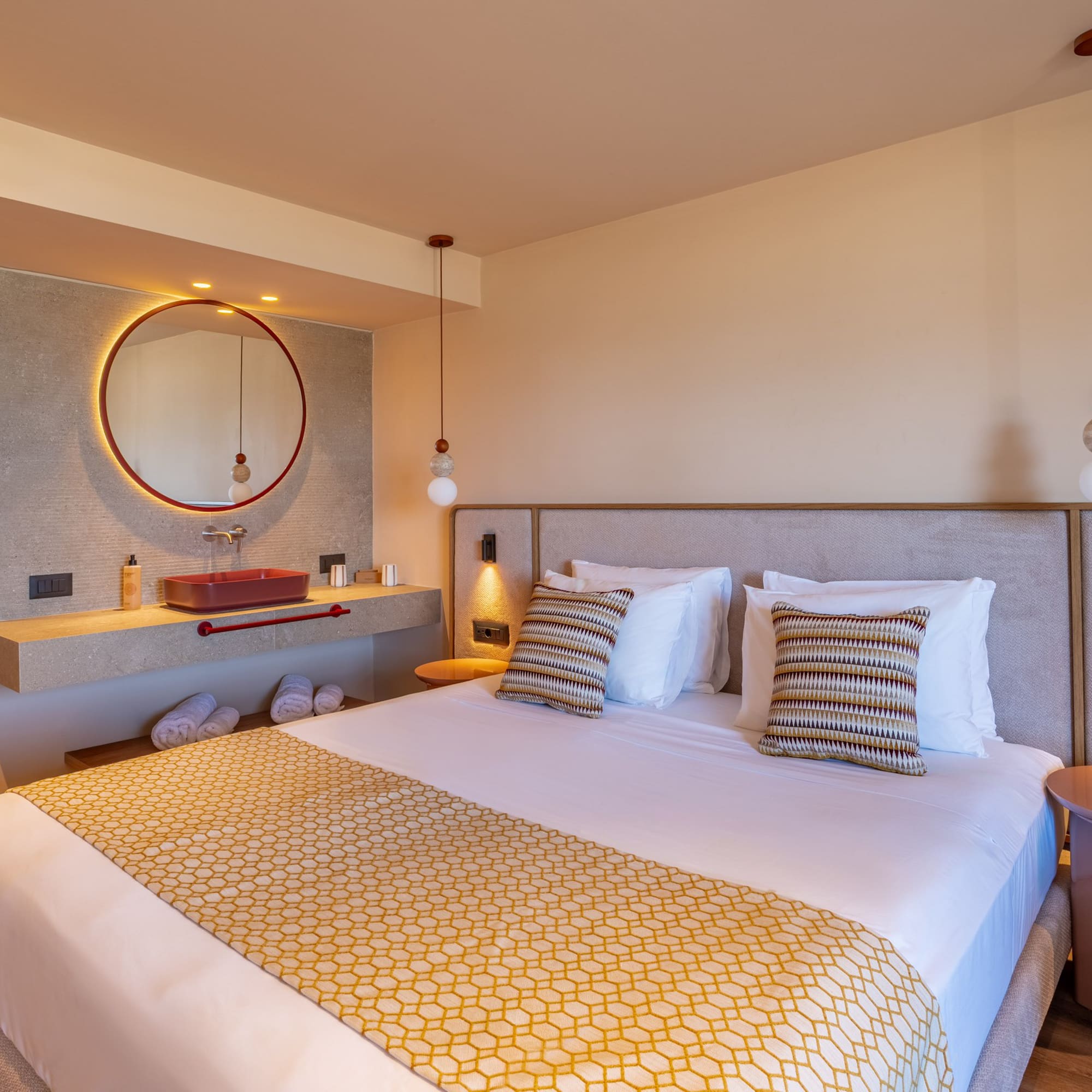 Luxurious modern hotel room with king bed, red vanity sink, and round backlit mirror.