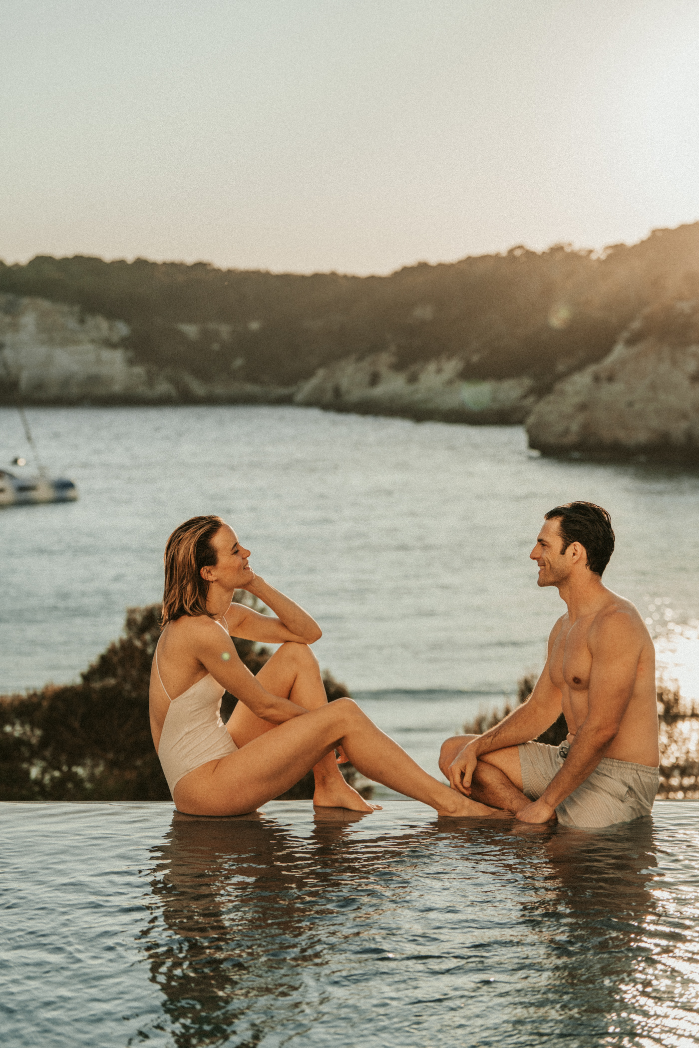Couple at infinity pool edge with ocean view at sunset.