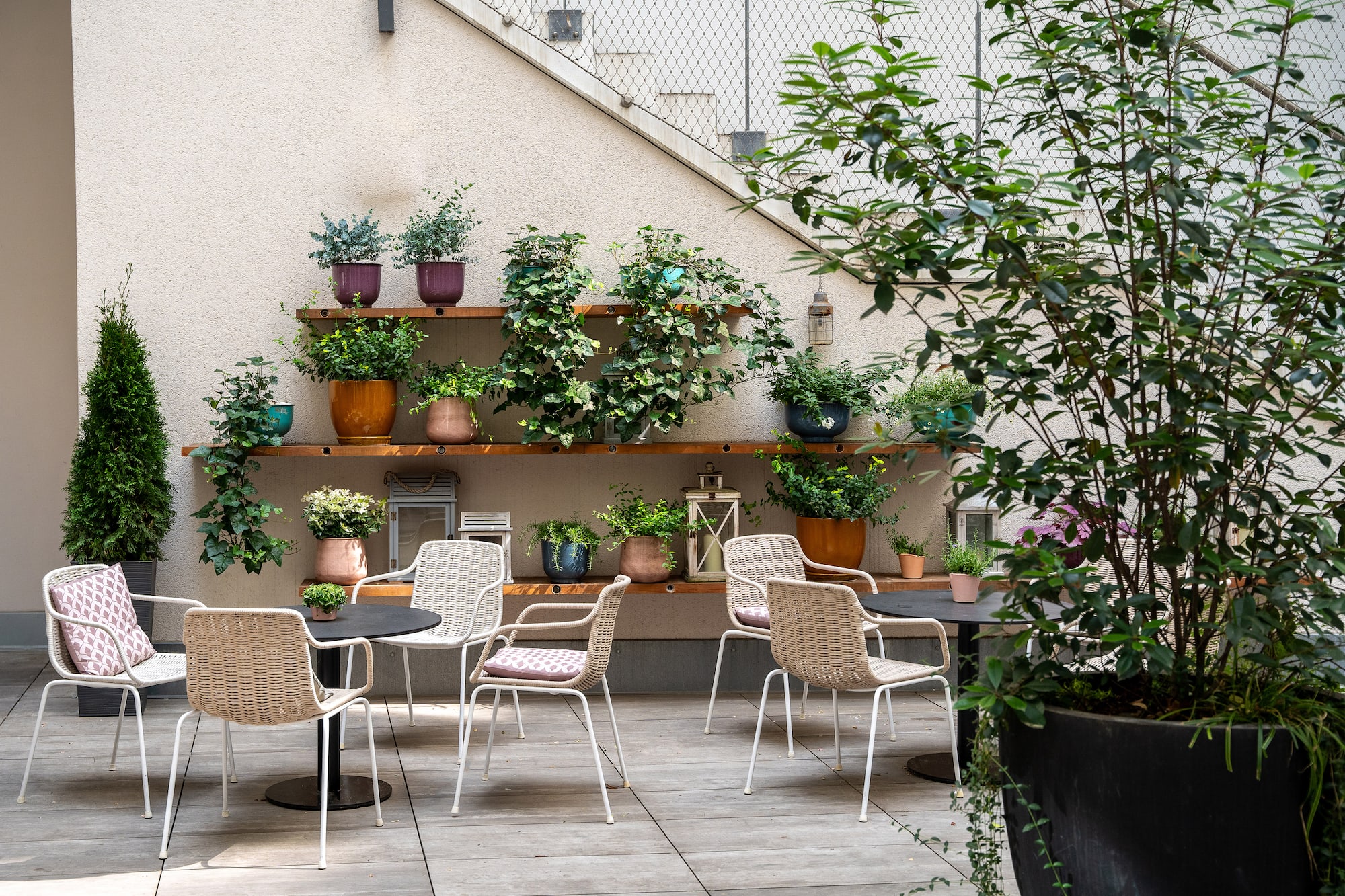 Modern patio with wicker chairs, tables, and abundant potted plants.