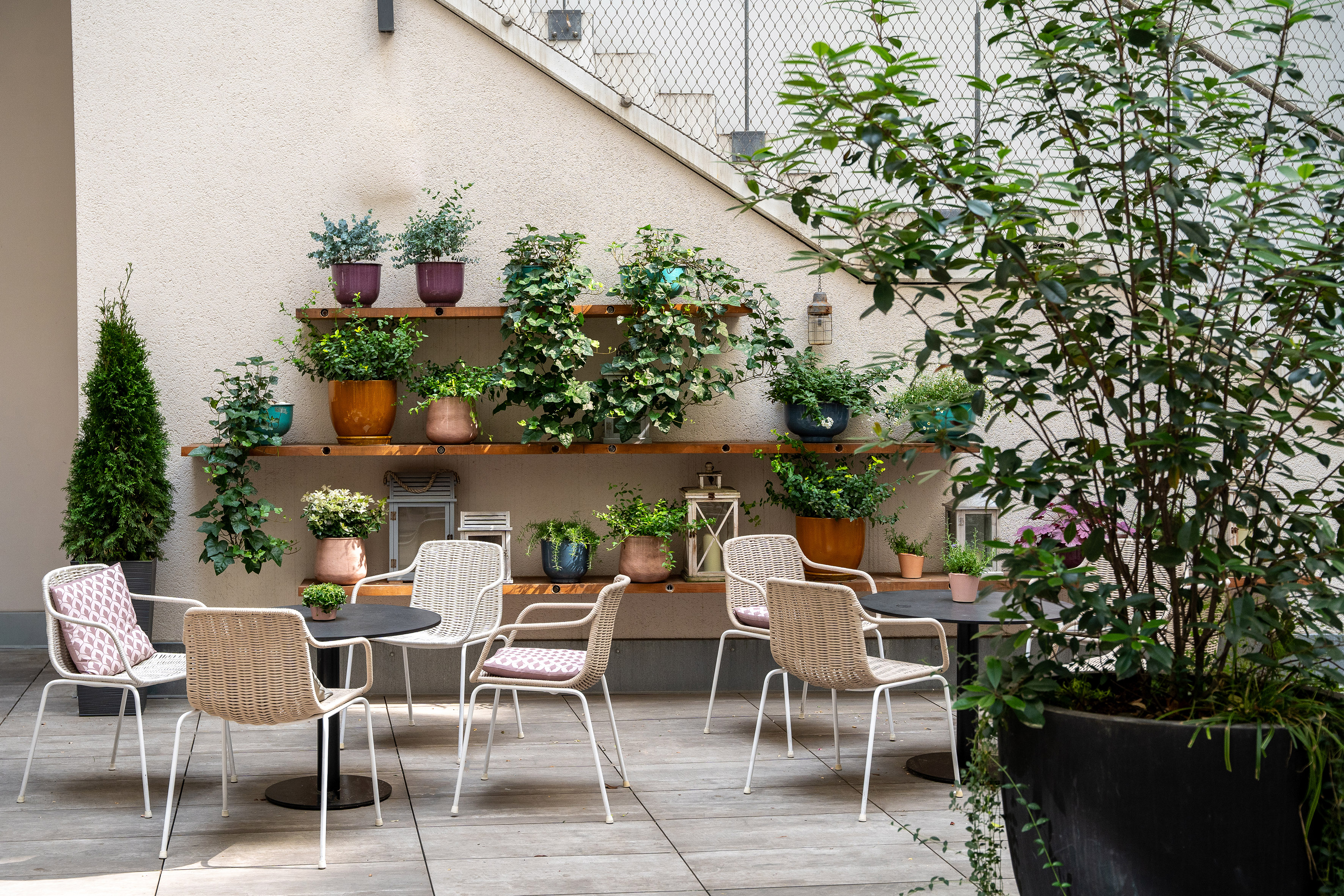 Modern patio with wicker chairs, tables, and abundant potted plants.