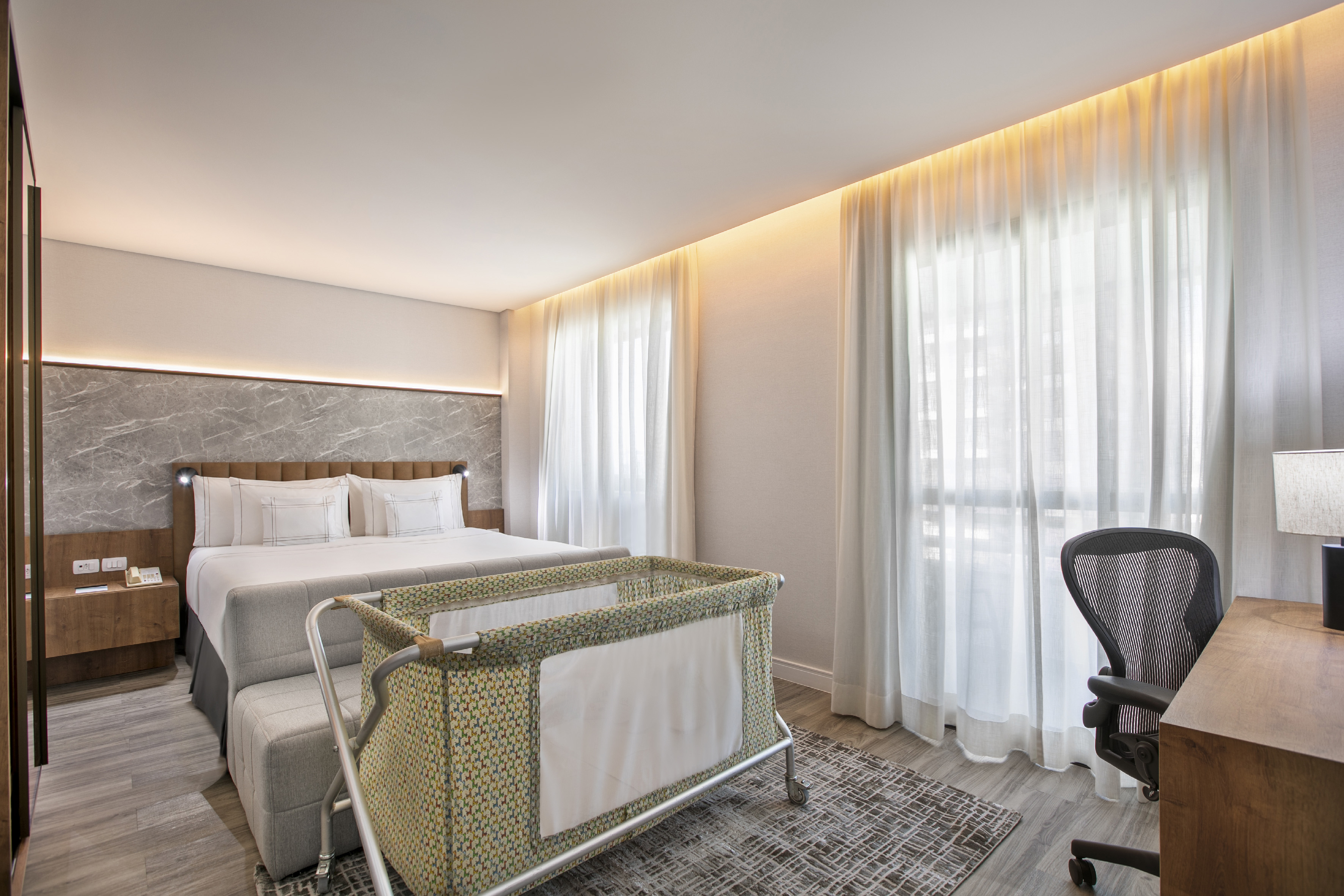 Family-friendly hotel room with queen bed, modern decor, and baby crib.