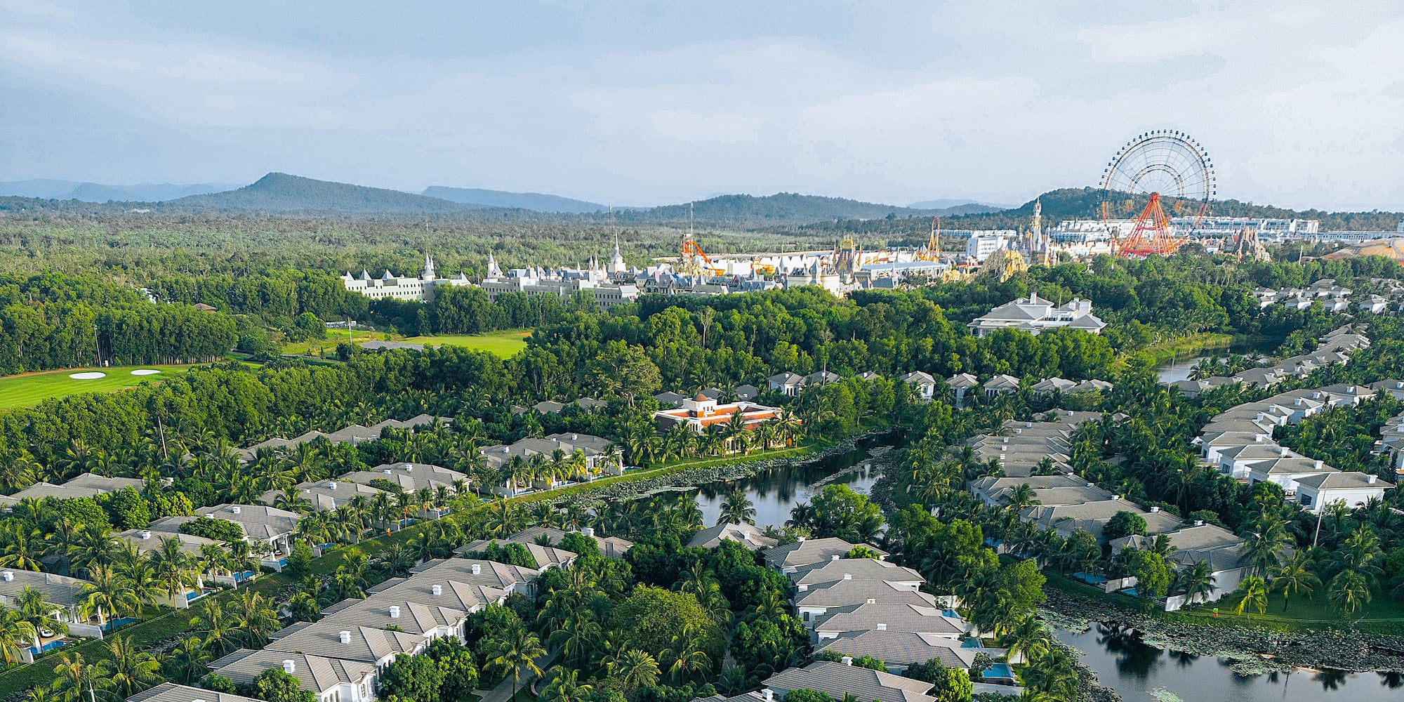 Aerial tropical resort, luxury villas, golf course, lake, theme park Ferris wheel.